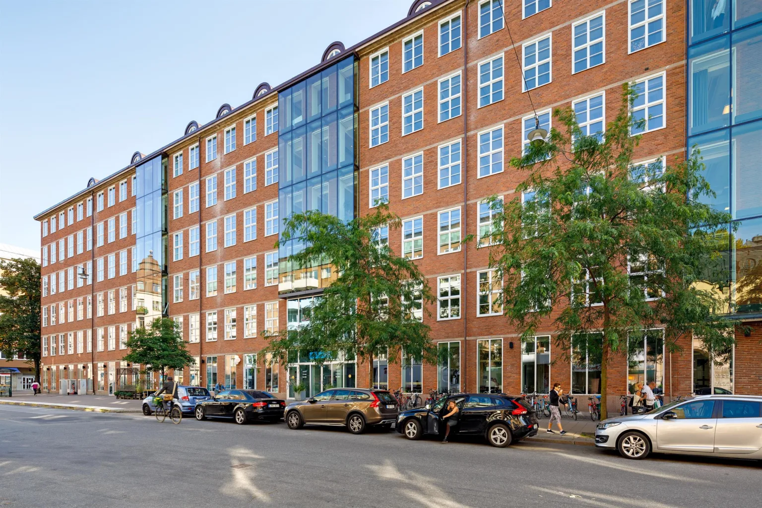3. En röd tegelbyggnad med stora fönster och parkerade bilar längs gatan.