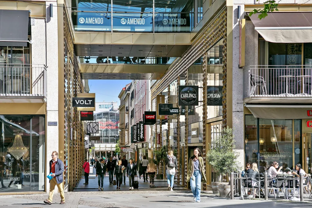 Ett köpcentrum med glasöverbyggnad, butiker och människor som promenerar.