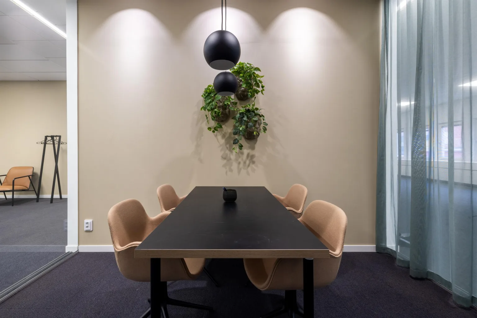 3. Mötesrum med ett svart bord, beige stolar och en hängande växtdekoration under tre spotlights.