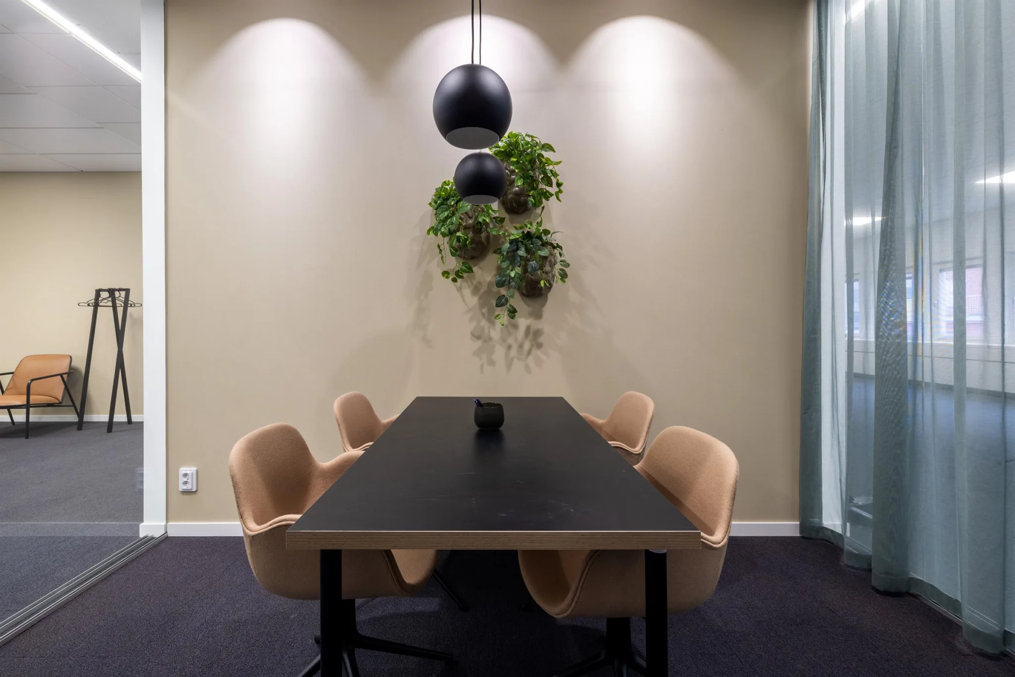 3. Mötesrum med ett svart bord, beige stolar och en hängande växtdekoration under tre spotlights.