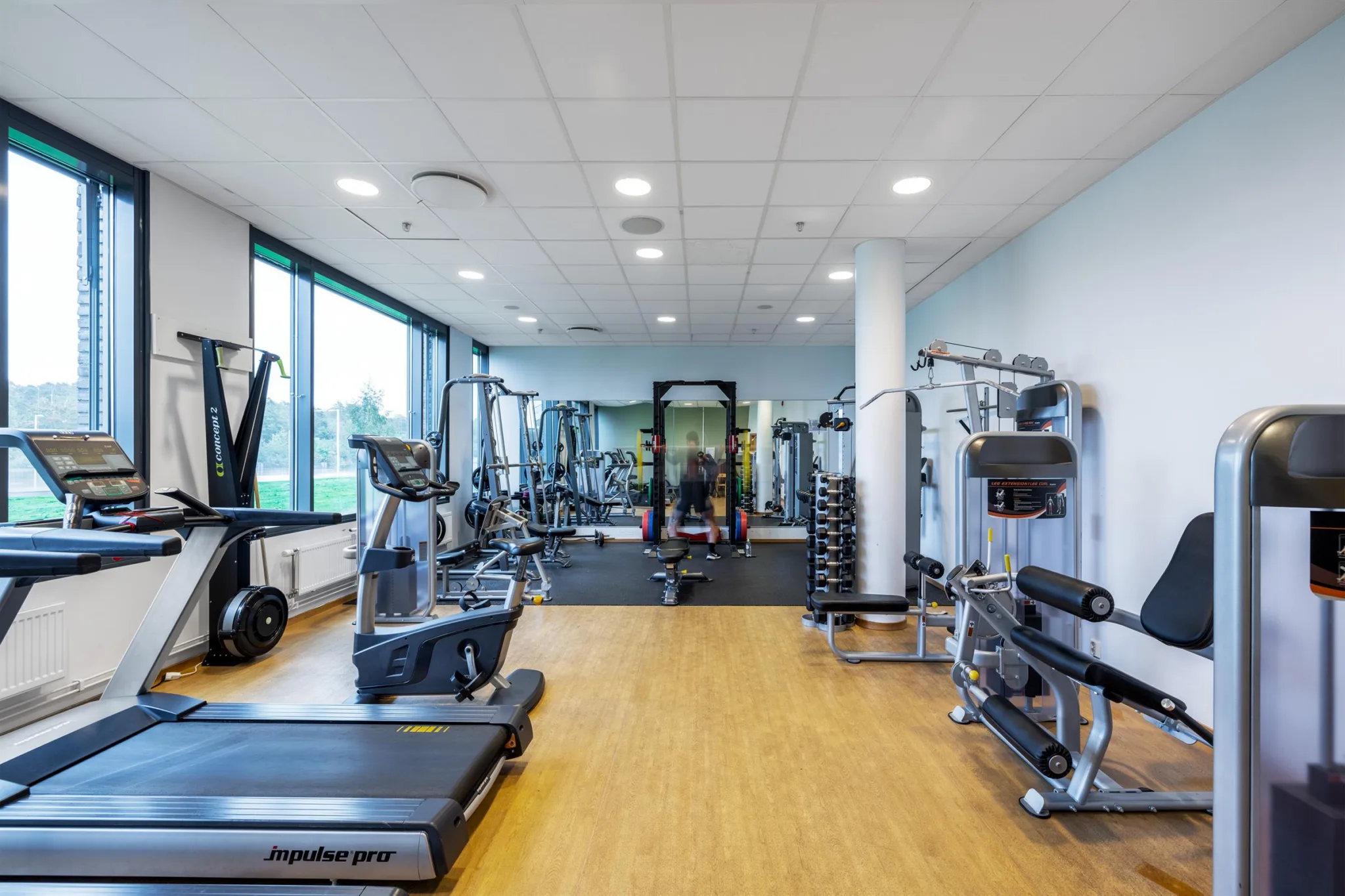 Ett gym med träningsutrustning, inklusive löpband, vikter och maskiner, på ett trägolv.