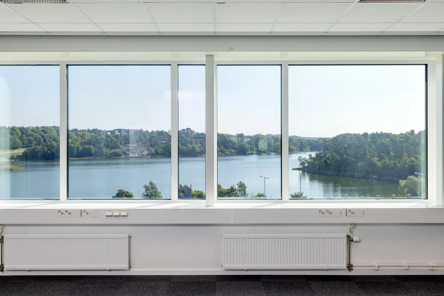 1. Utsikt genom stora fönster mot en bred flod omgiven av grönska.