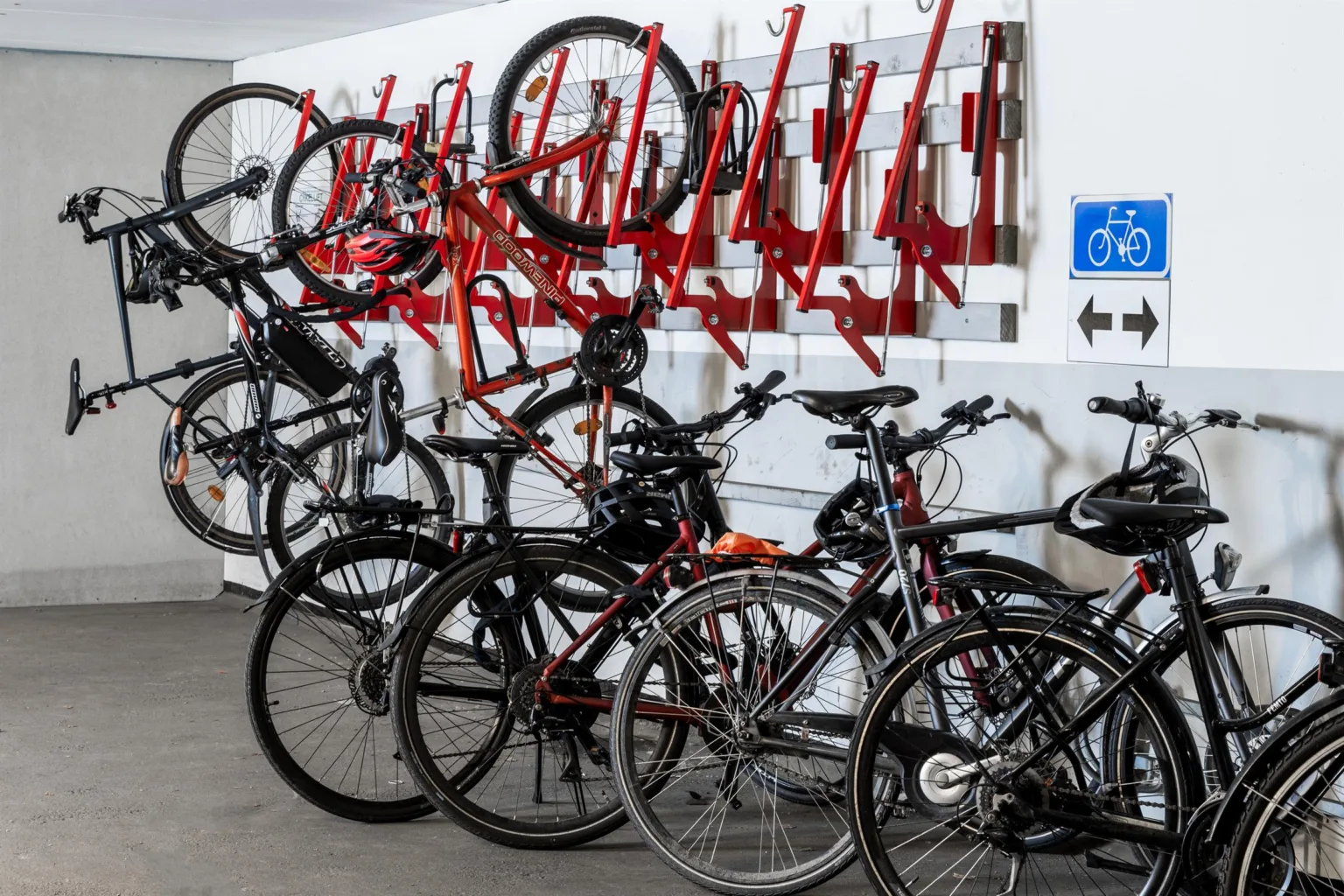 Cyklar parkerade på röda cykelställ i en inomhusmiljö, med en handikappsymbol på väggen.
