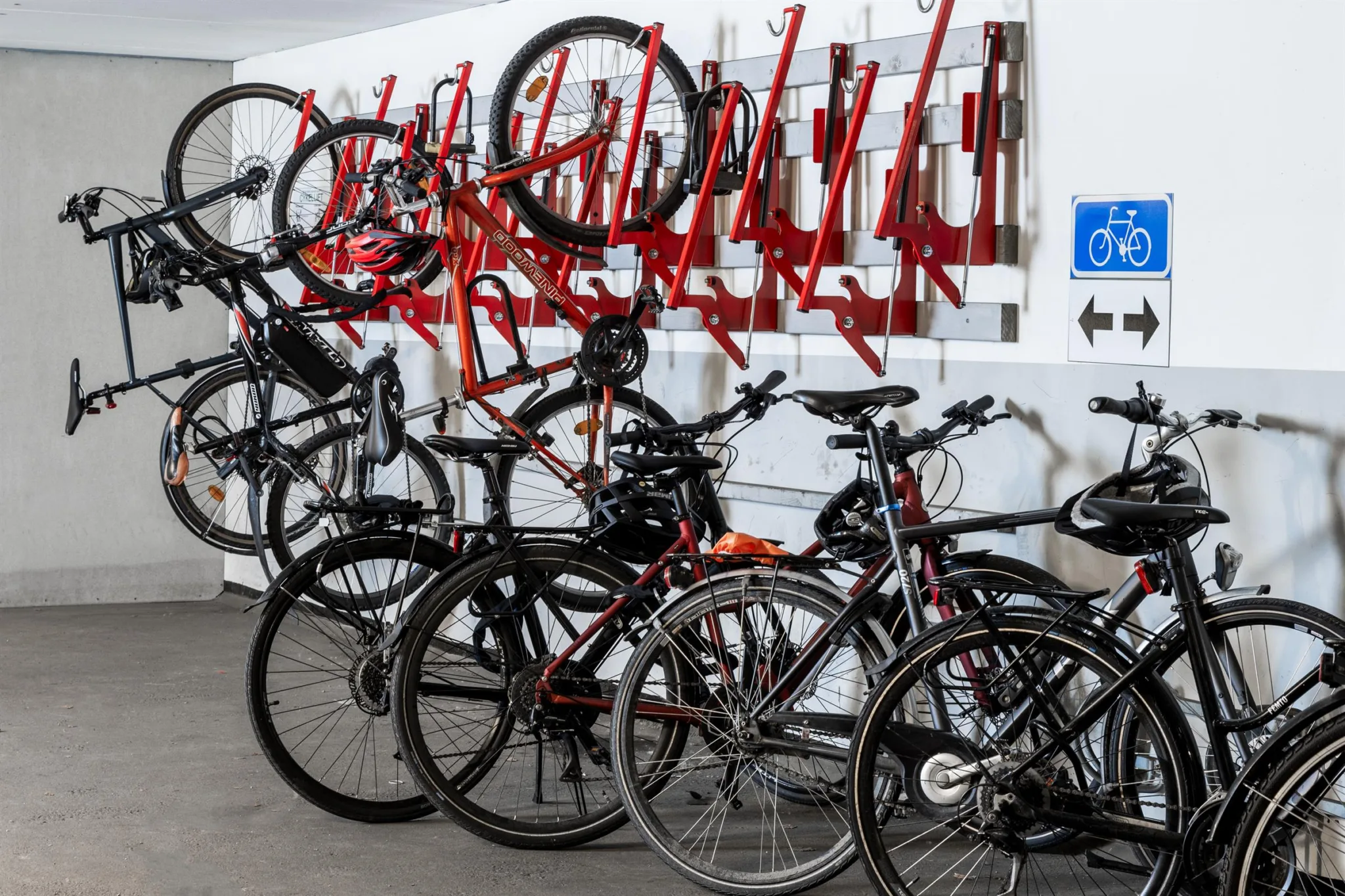 Cyklar parkerade på röda cykelställ i en inomhusmiljö, med en handikappsymbol på väggen.