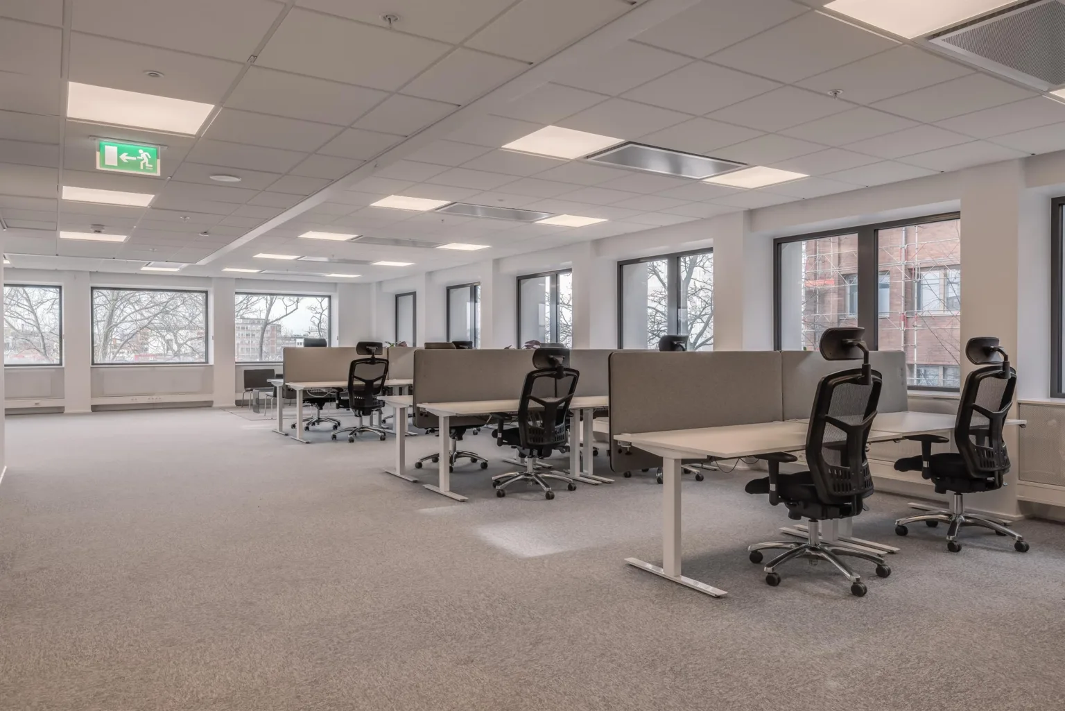 Ett rymligt kontor med skrivbord, kontorsstolar och fönster som vetter mot en stadsmiljö.