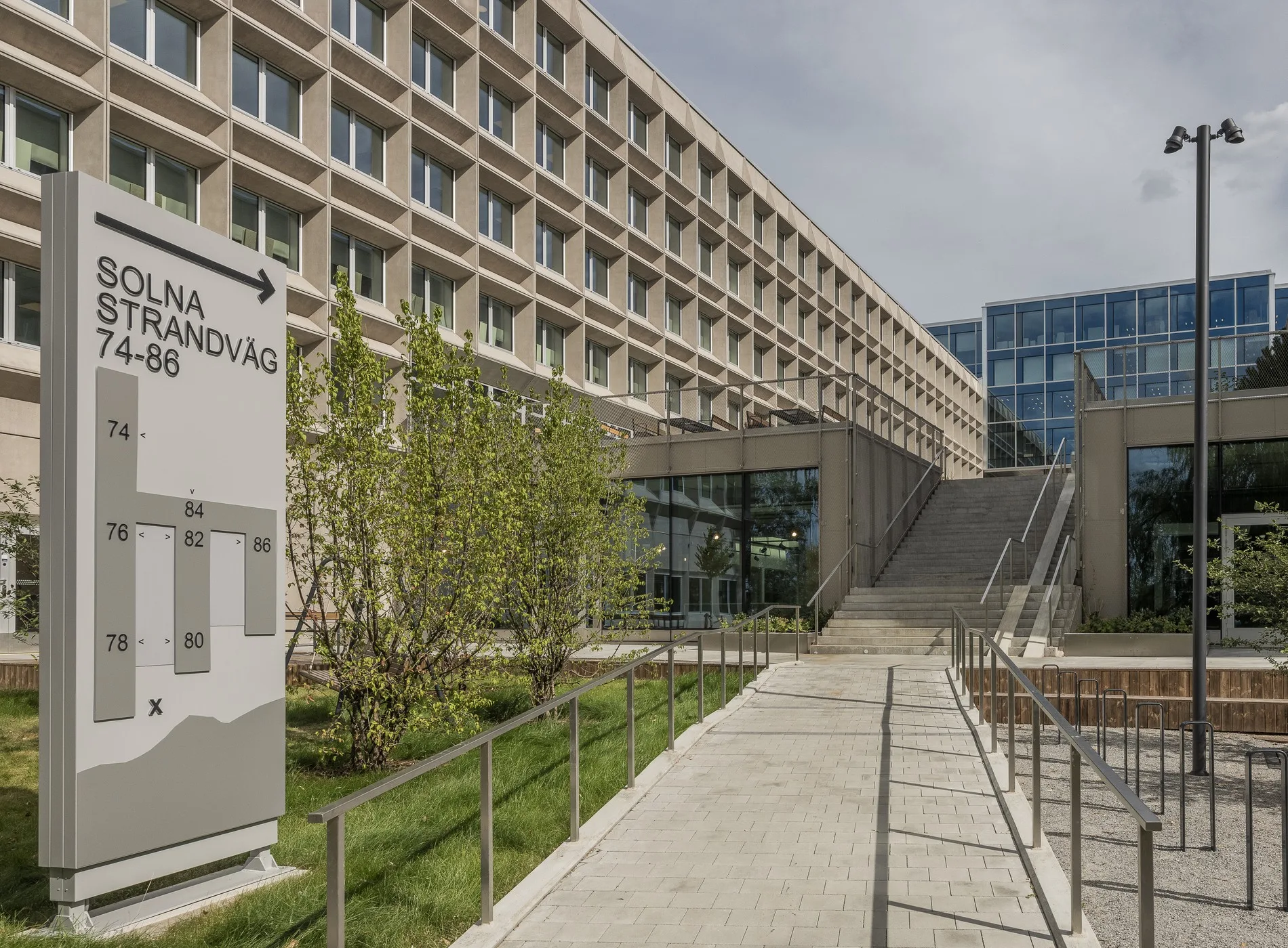 En byggnadsentré med en skylt som visar riktning till "Aula Medica", omgiven av grönska och modern arkitektur.
