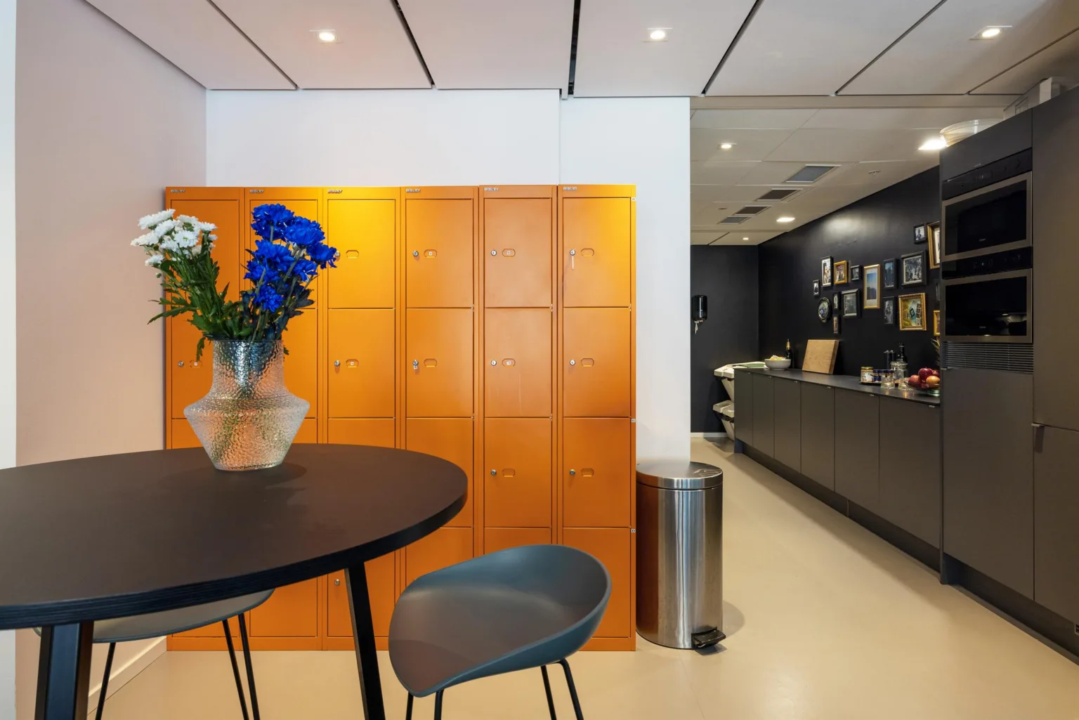 Ett runt bord med en vas med blommor framför en orange skåpvägg och en reception i bakgrunden.