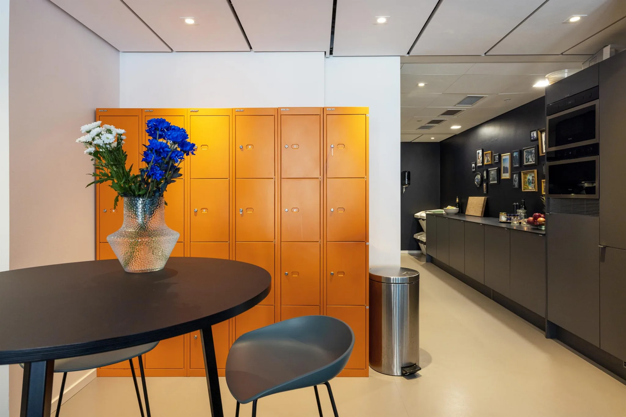 Ett runt bord med en vas med blommor framför en orange skåpvägg och en reception i bakgrunden.