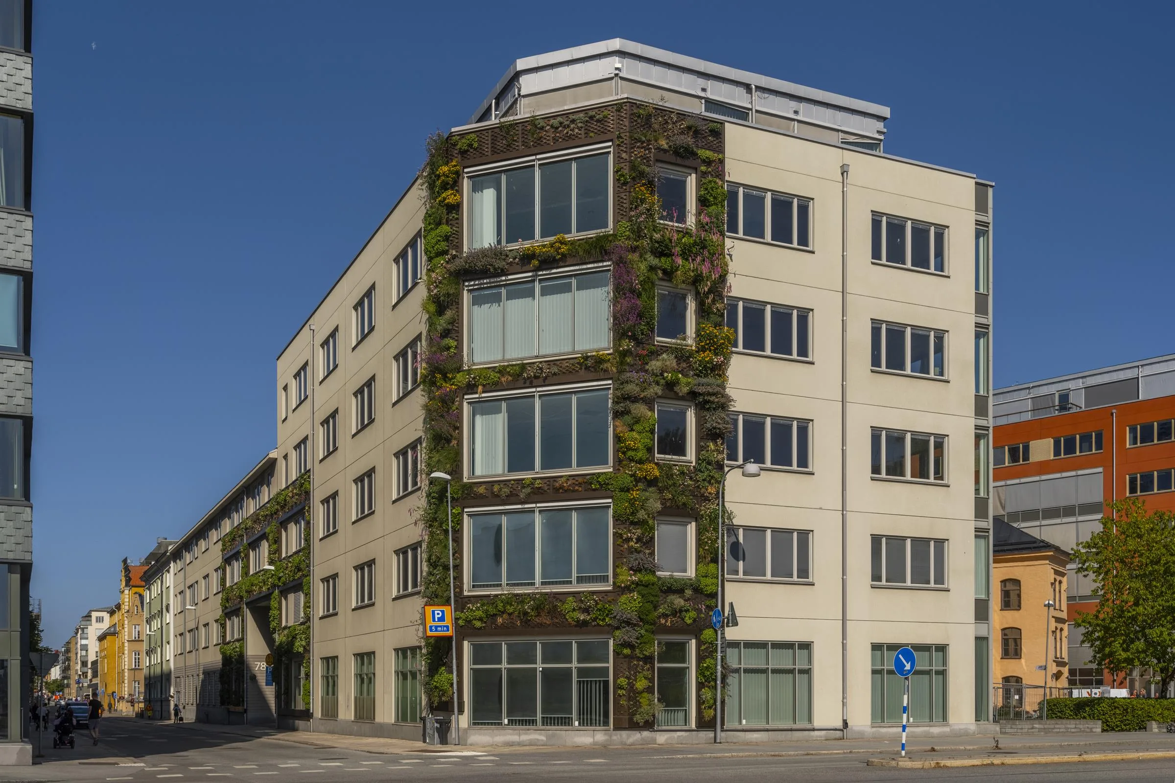 5. En beige byggnad med gröna växtpaneler på fasaden och stora fönster, belägen vid en korsning.
