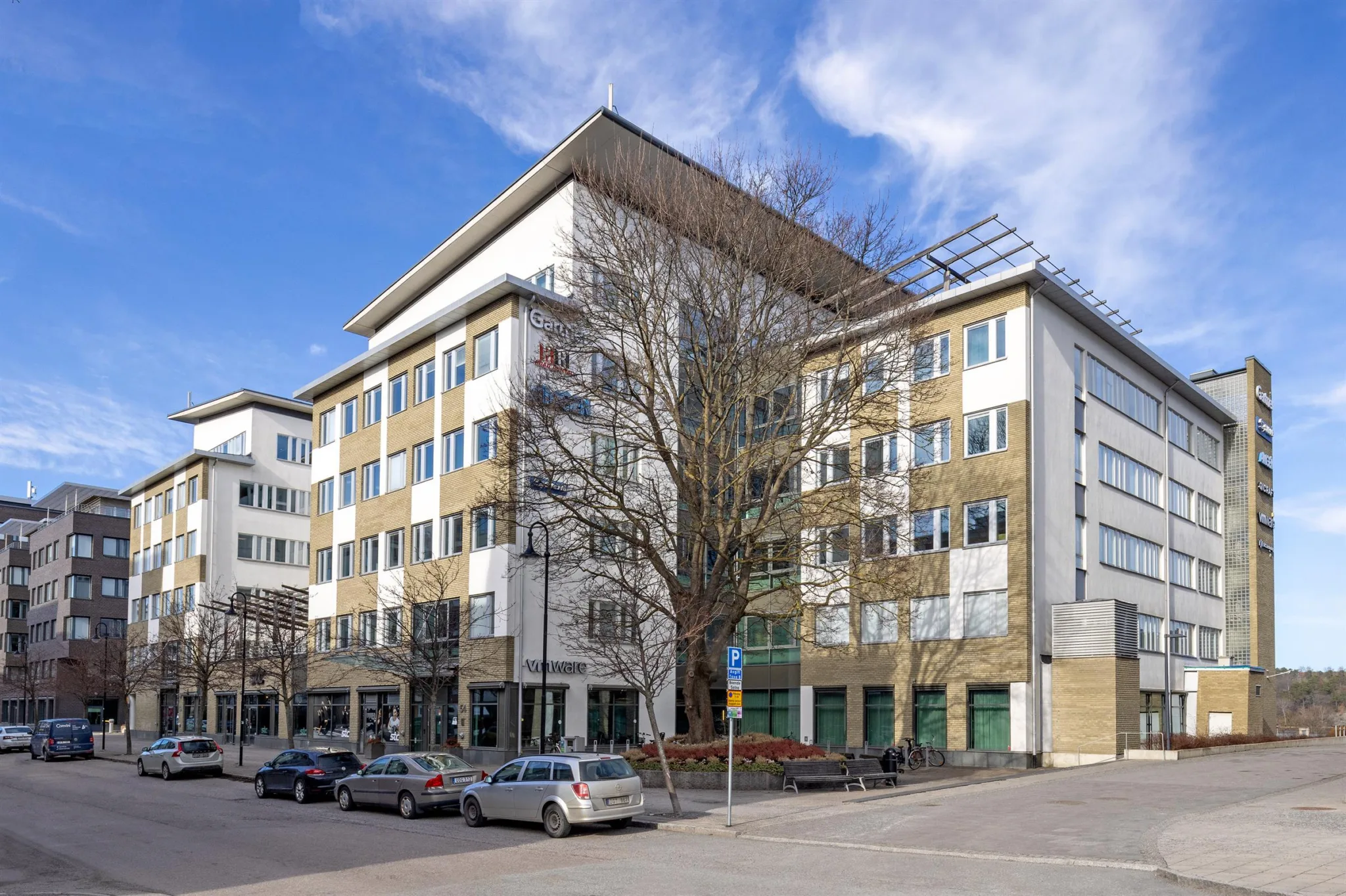 2. En flerbyggnad i modern stil med vita och beige fasader, omgiven av bilar och ett träd.