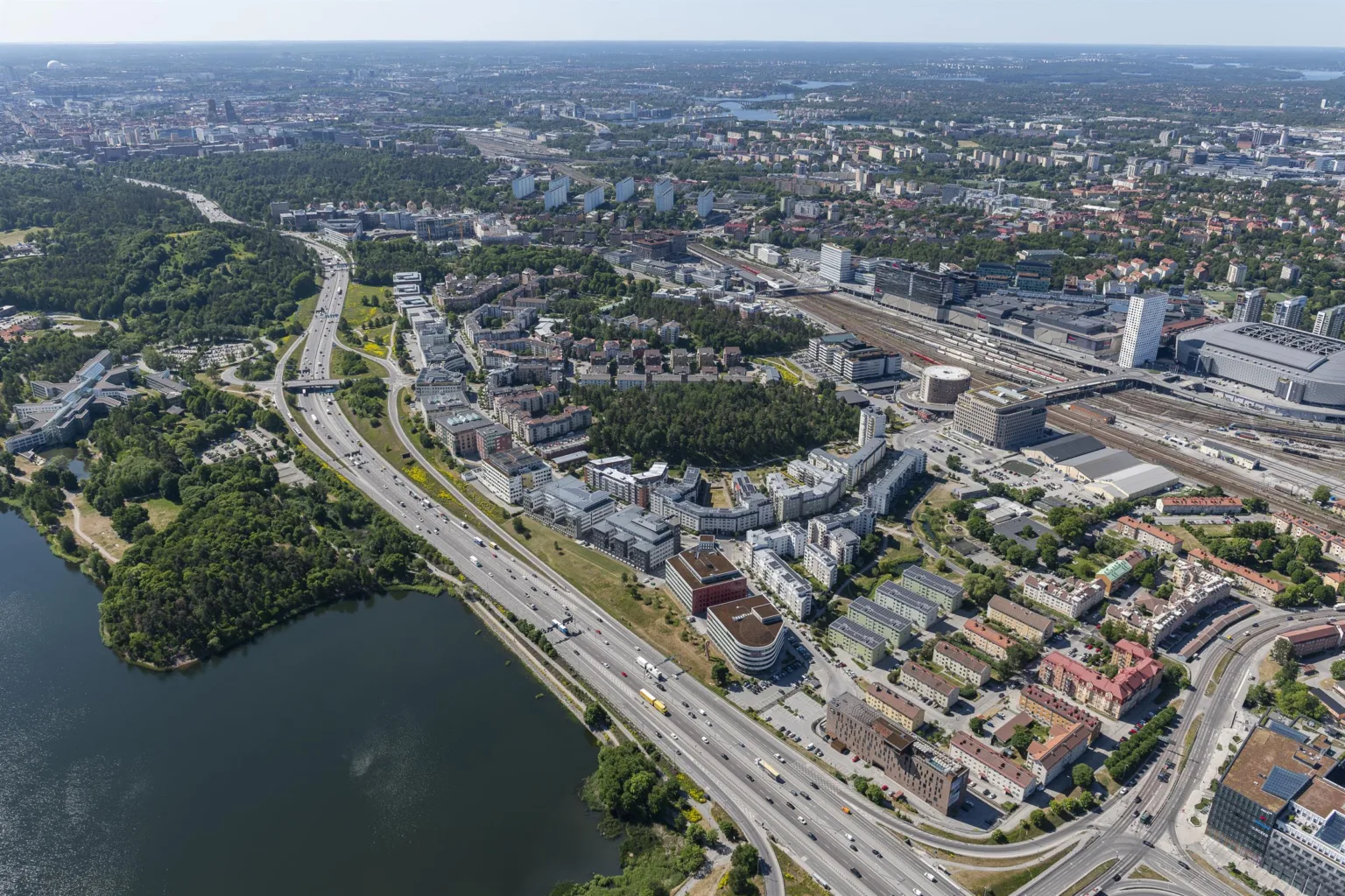 4. Flygvy av ett stadsområde med vägar, byggnader, grönområden och en sjö.