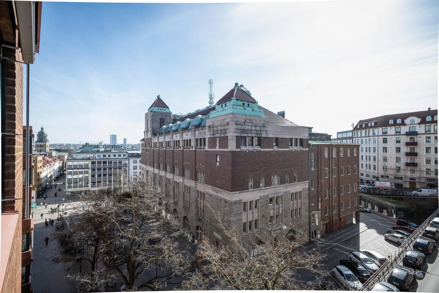 En stor byggnad i sten med gröna takdetaljer, omgiven av stadsmiljö och träd.