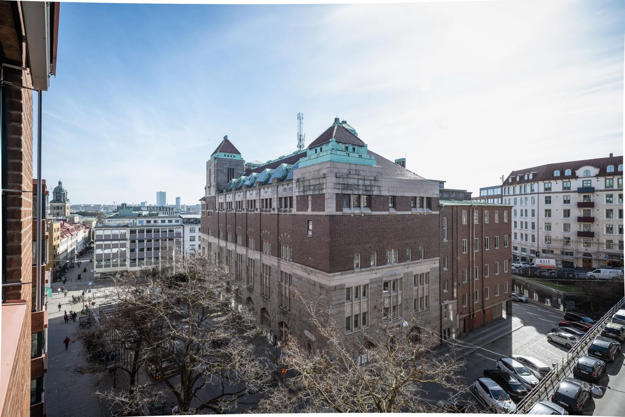 En stor byggnad i sten med gröna takdetaljer, omgiven av stadsmiljö och träd.