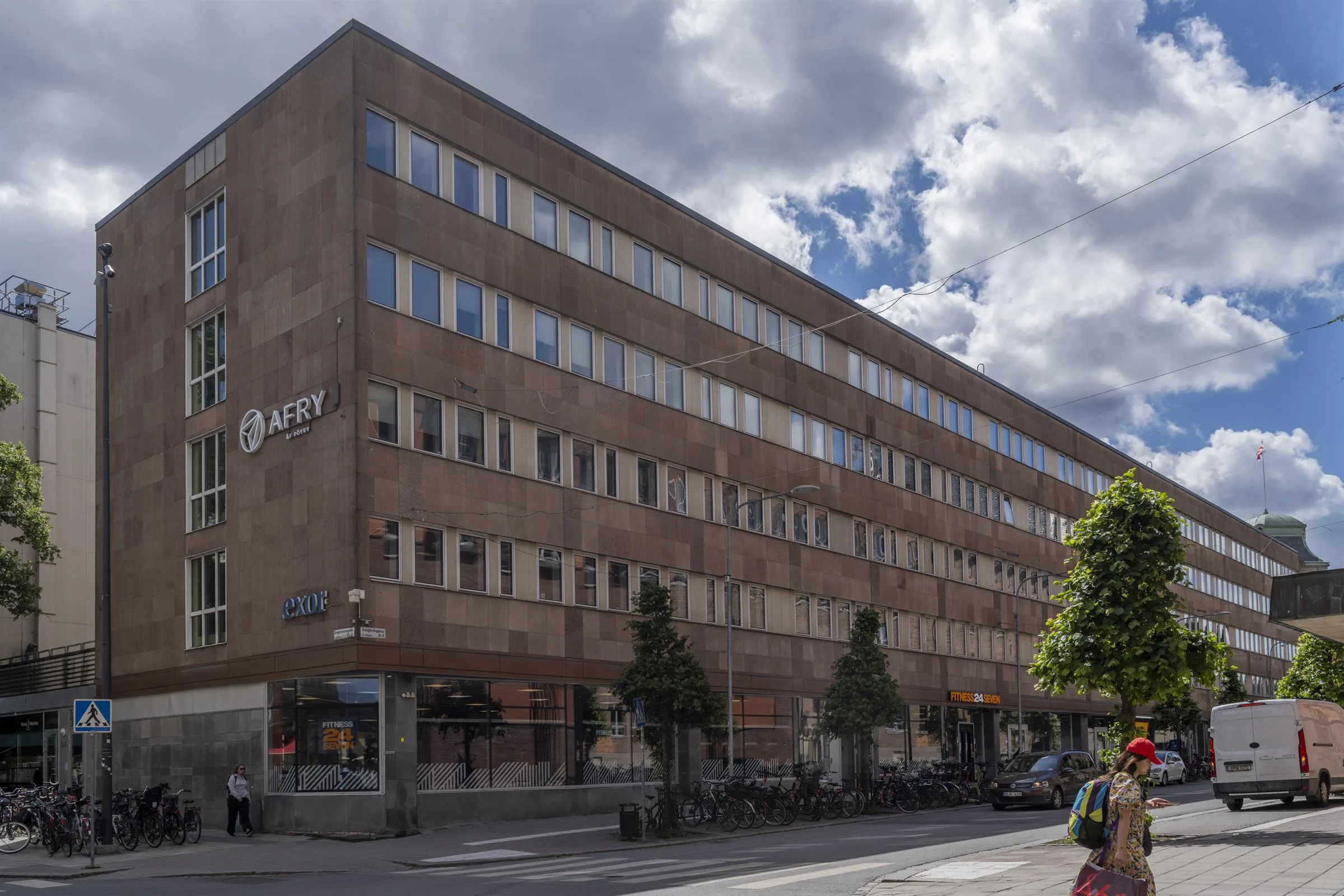 1. Ett stort fyravåningshus i tegel med många fönster, en blå himmel med moln i bakgrunden.