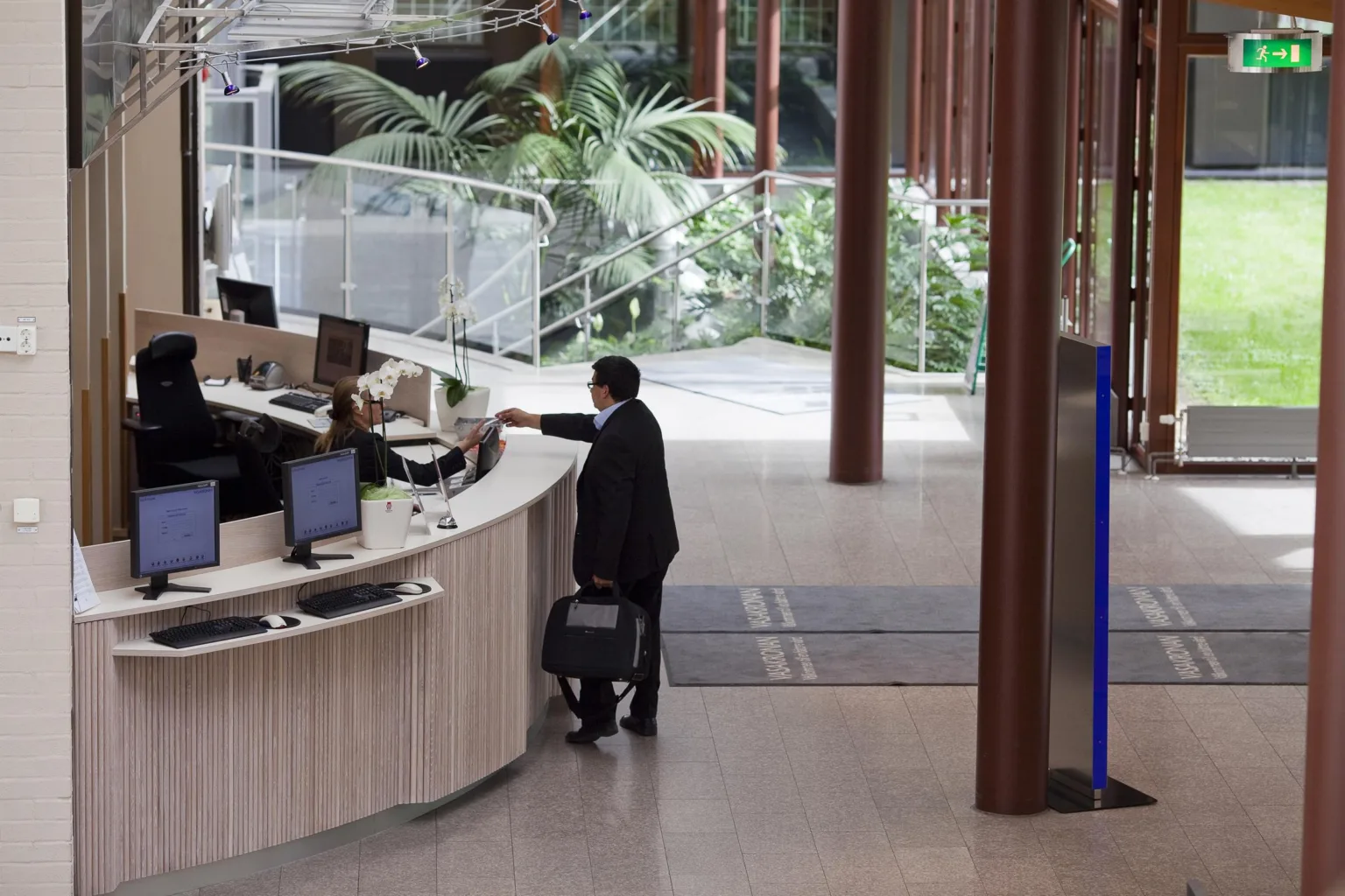 2. Man i kostym med portfölj vid en receptionsdisk i en ljus och modern miljö med växter i bakgrunden.