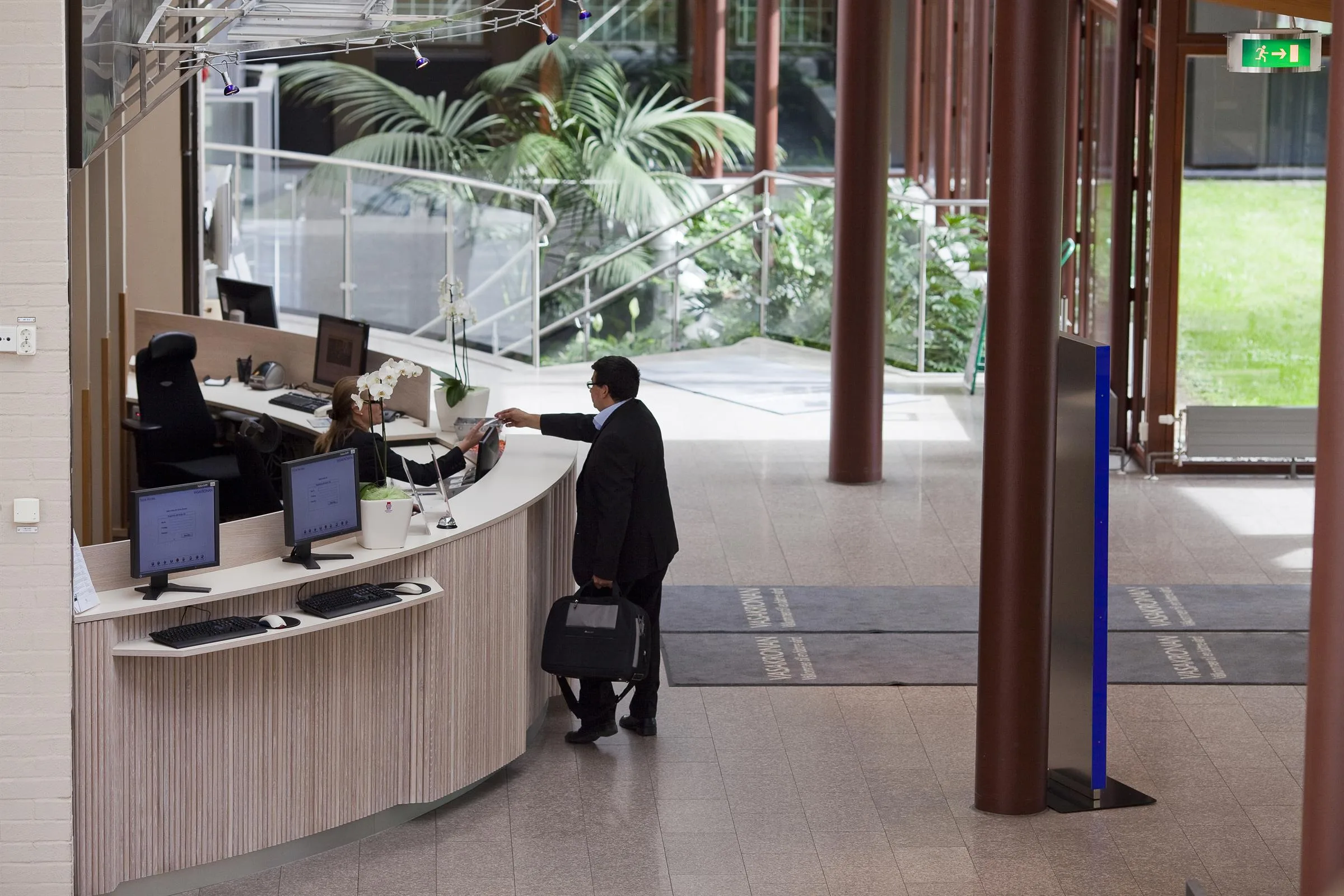 2. Man i kostym med portfölj vid en receptionsdisk i en ljus och modern miljö med växter i bakgrunden.