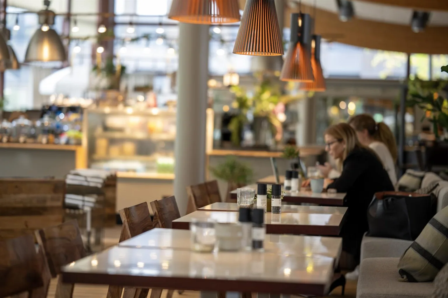 3. Restaurangmiljö med personer som sitter vid bord under hängen av kopparfärgade lampor, med fokus på mat och dryck.