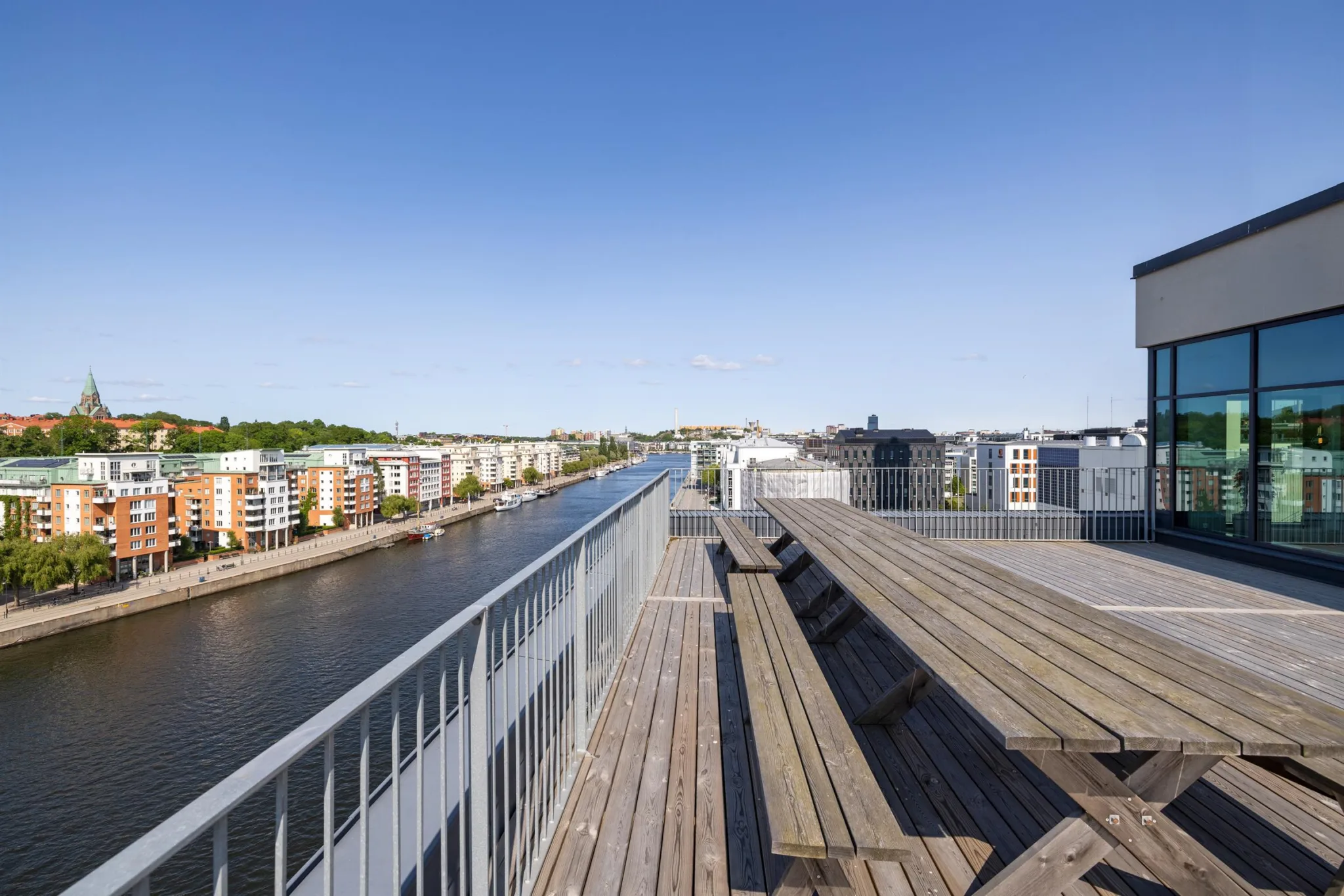 En takterrass med träbänkar och utsikt över en vattenkanal och omgivande byggnader.