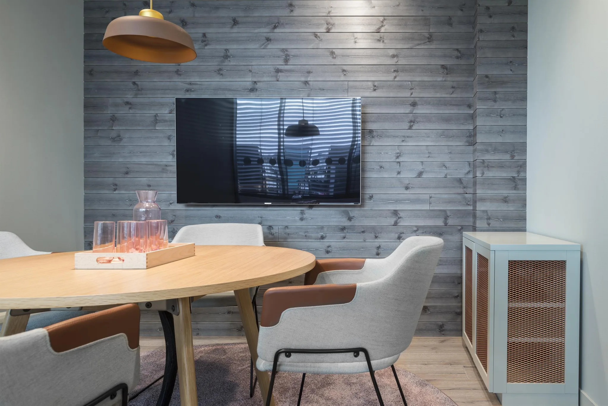 5. Ett mötesrum med ett runt träbord, bekväma stolar, en väggmonterad TV och väggar i träpanel.