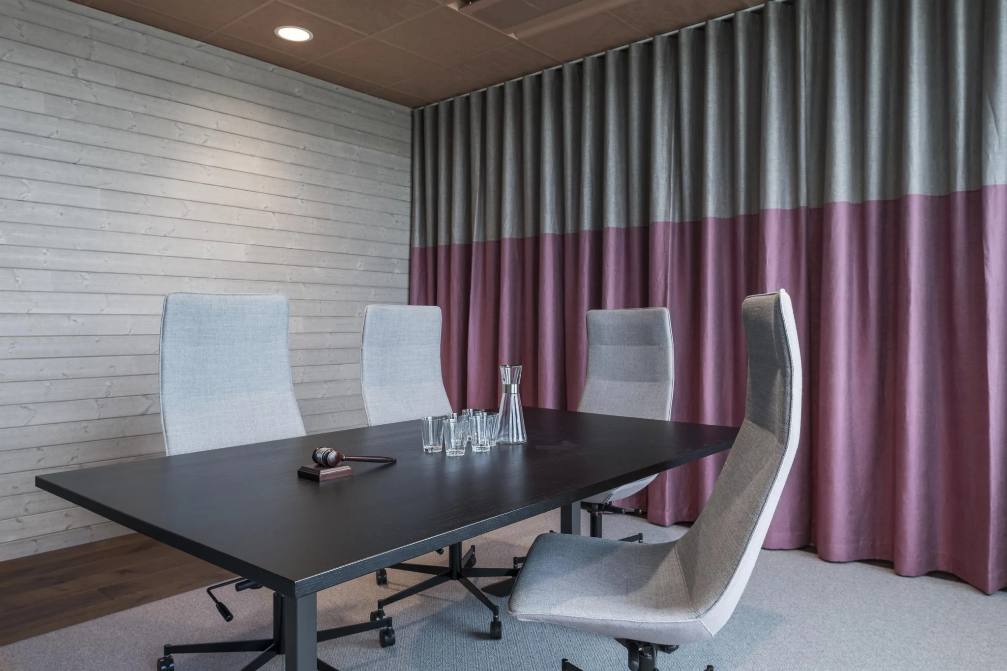 4. Ett mötesrum med ett svart bord, fyra vita stolar och gardiner i två färger, rosa och grått.