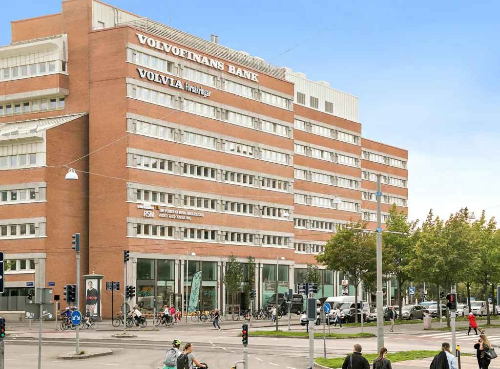 1. En stor tegelbyggnad med flera våningar, texten "Vasaterminalen Gatuplan" syns högst upp, omgiven av träd och fotgängare.