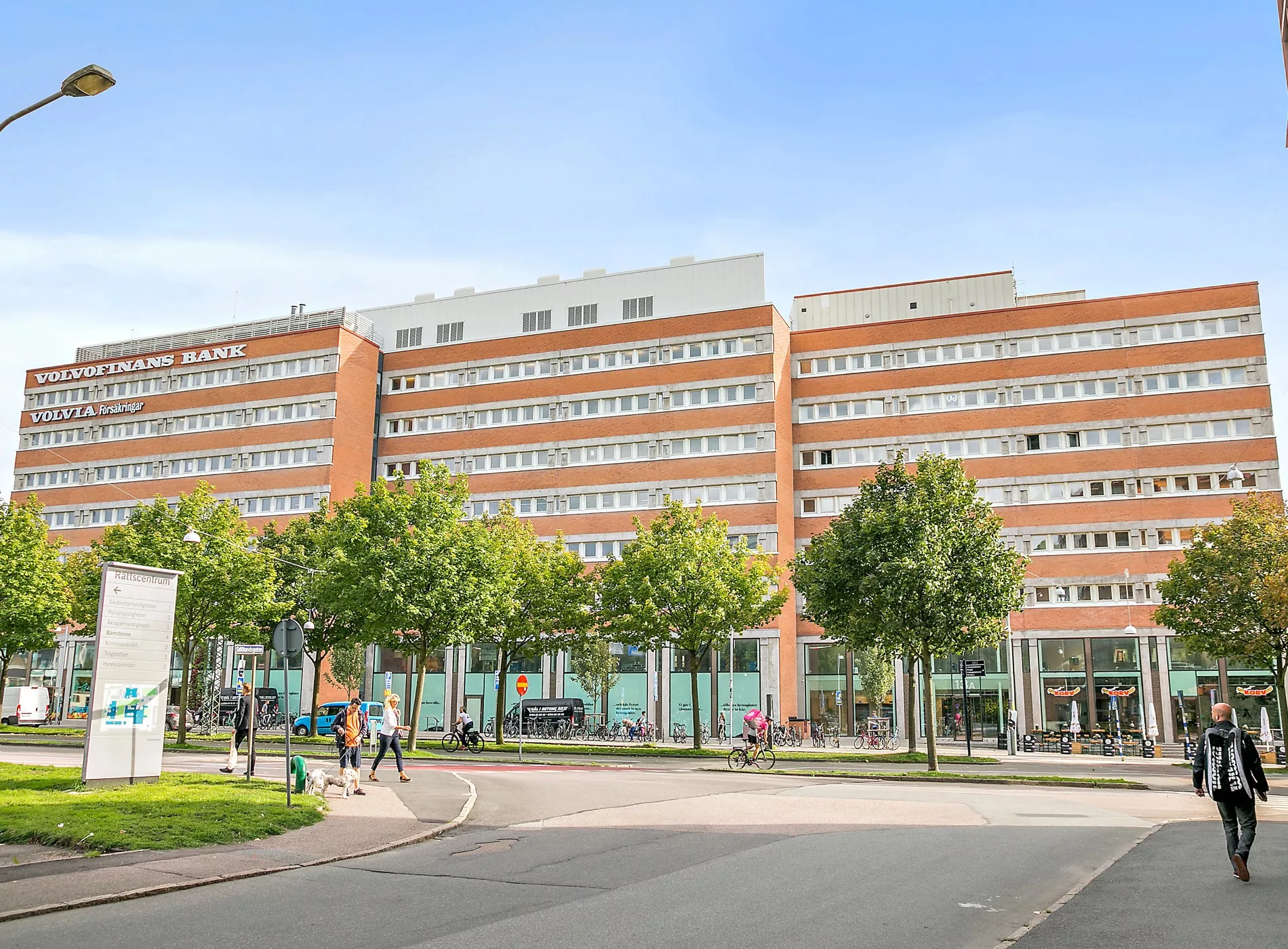 4. En bred tegelbyggnad med flera våningar, omgiven av en gata och grönområden med träd.