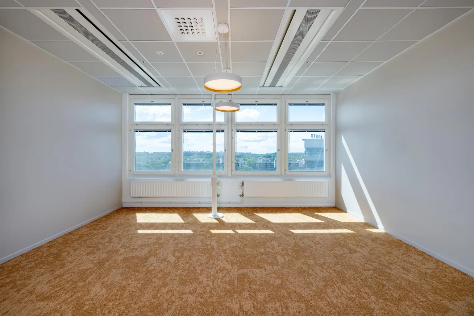 3. Ett ljust rum med stora fönster, gråa väggar och taklampor, samt beige matta på golvet.