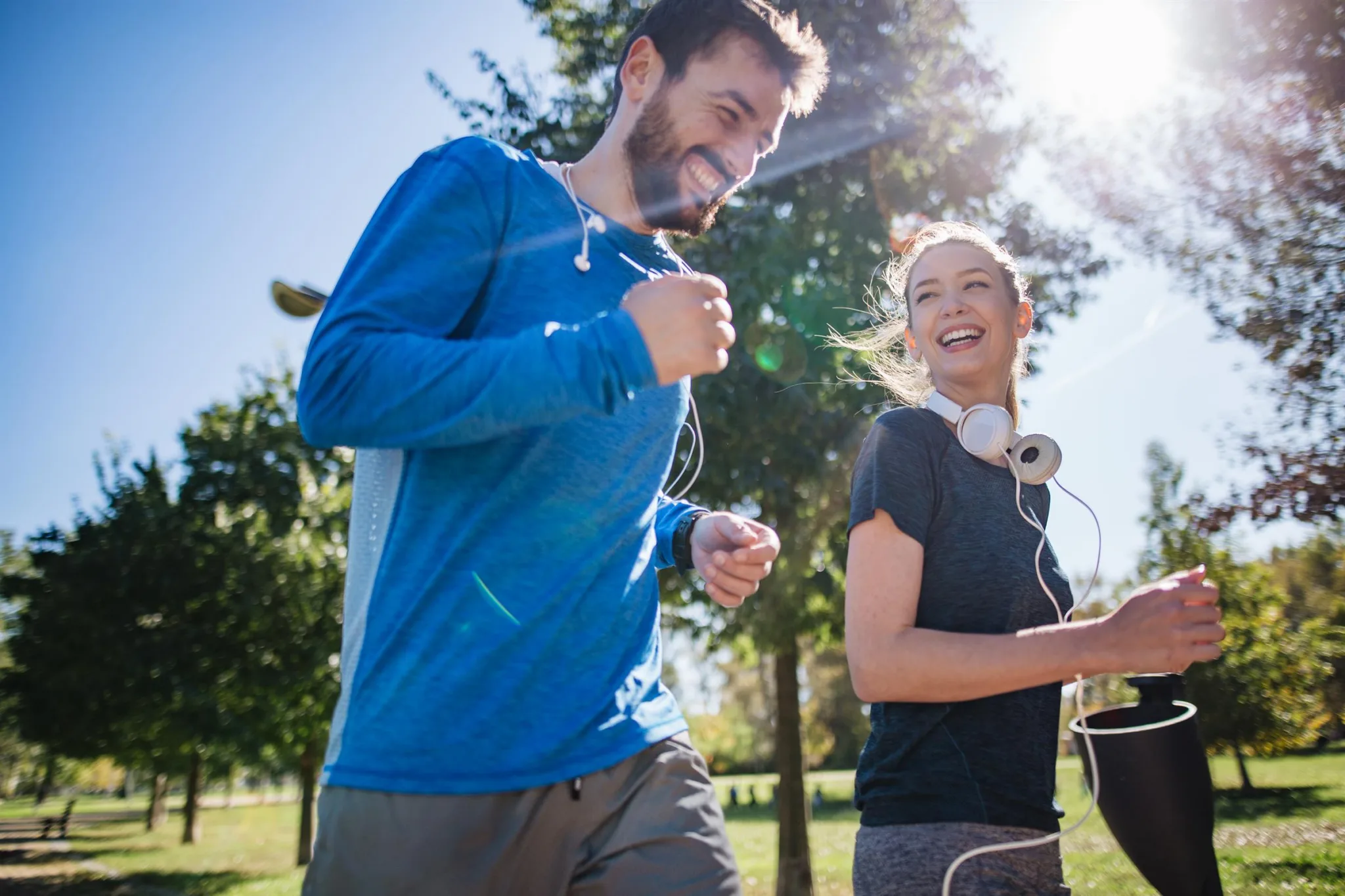 3. En man och kvinna joggar tillsammans i en park under soligt väder, leende mot varandra.