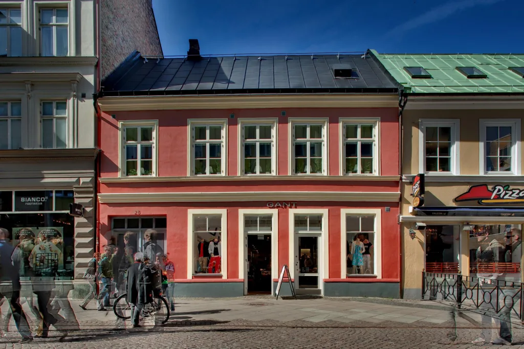 Ett mindre rosa hus med vita fönster och grönt tak, cyklar står parkerade utanför.