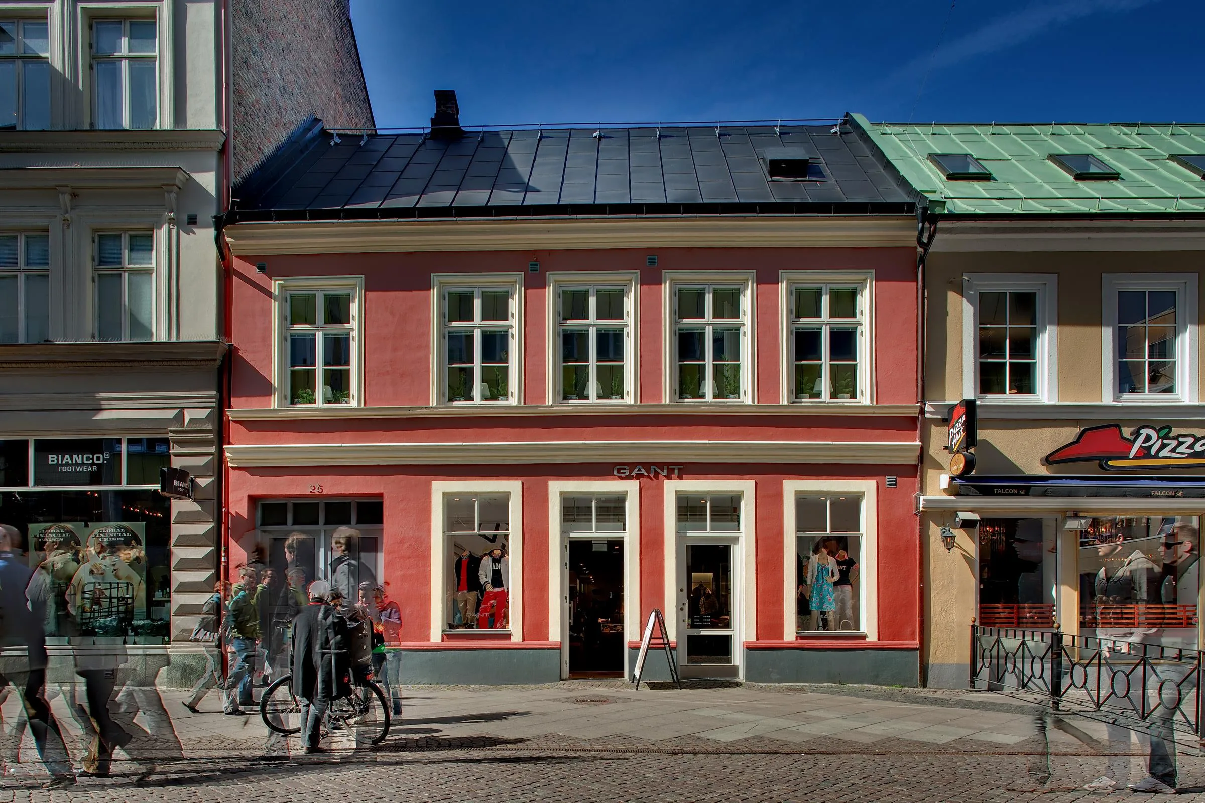 Ett mindre rosa hus med vita fönster och grönt tak, cyklar står parkerade utanför.