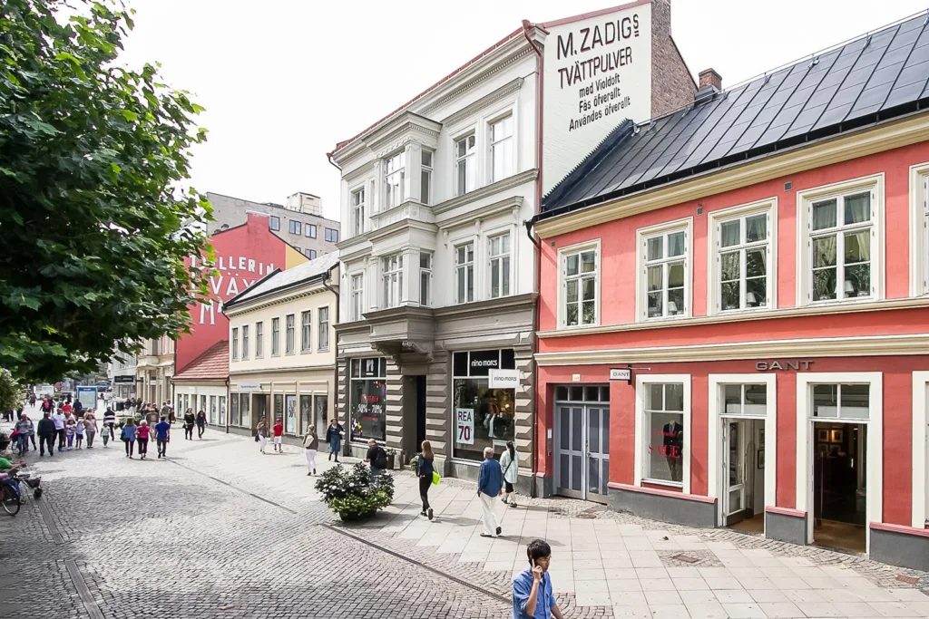 En kullerstensgata med flera äldre byggnader, en skylt på en av byggnaderna visar texten "M. Zackrisson Tapetserare".