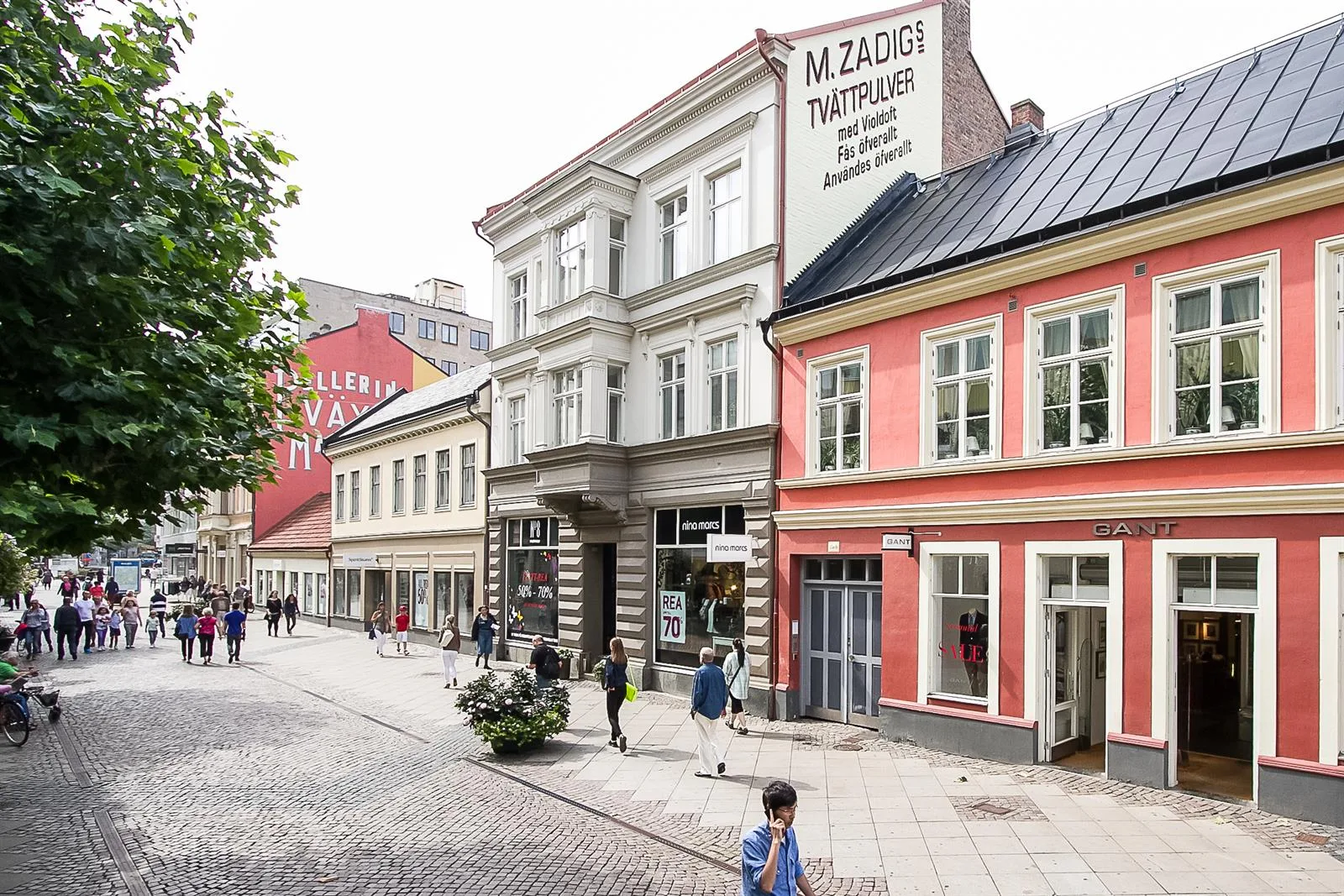 En kullerstensgata med flera äldre byggnader, en skylt på en av byggnaderna visar texten "M. Zackrisson Tapetserare".
