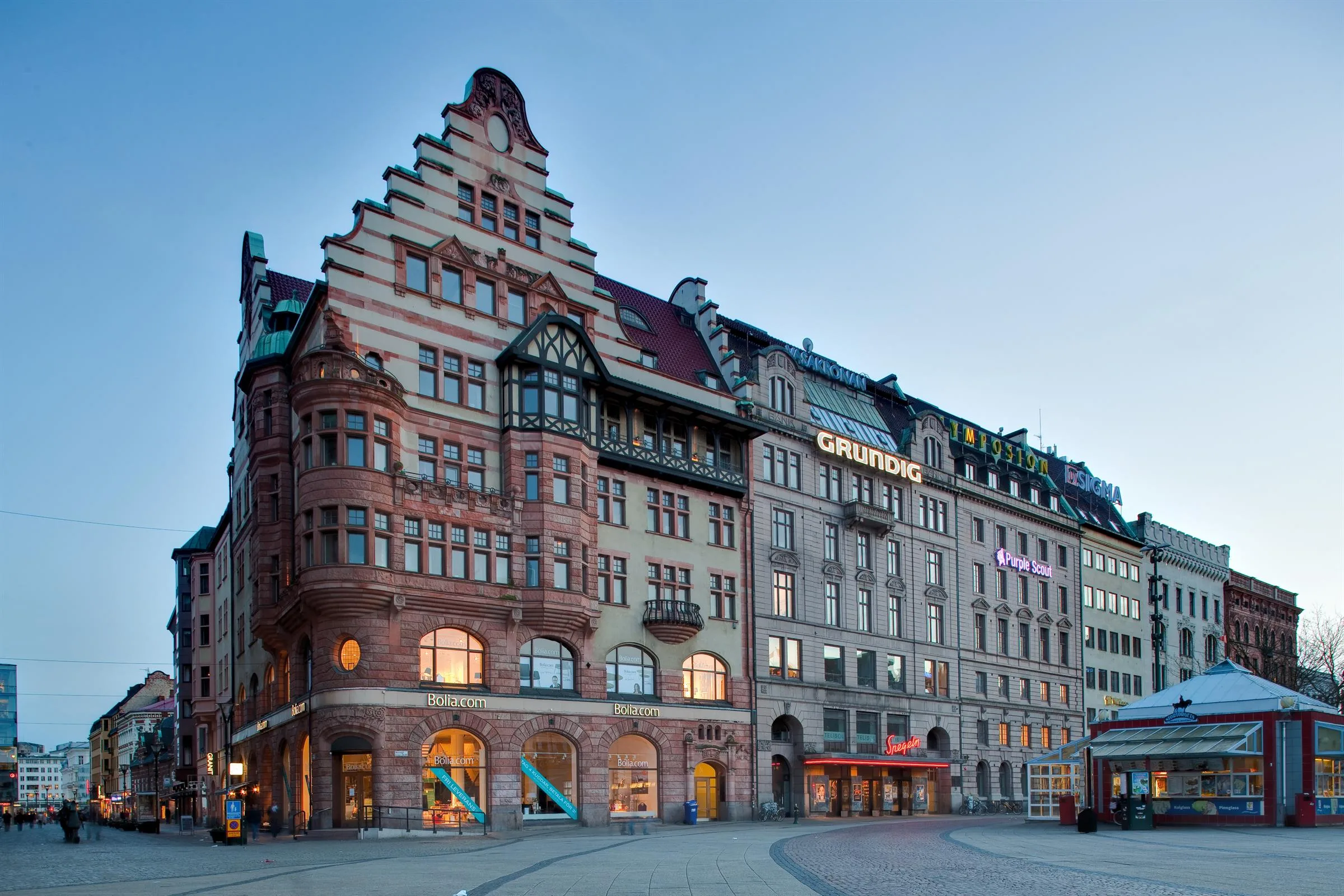En historisk byggnad med dekorativ fasad och trapptak, omgiven av andra byggnader i stadsmiljö.