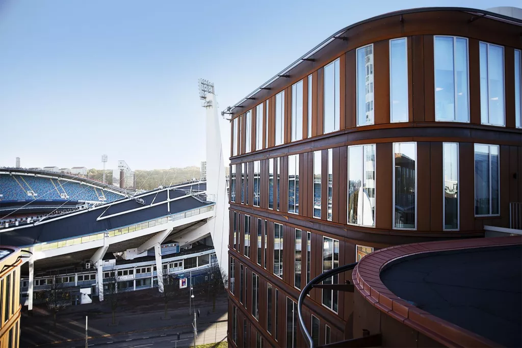3. En byggnad med glasfasad och rundad design, med en stadion i bakgrunden.