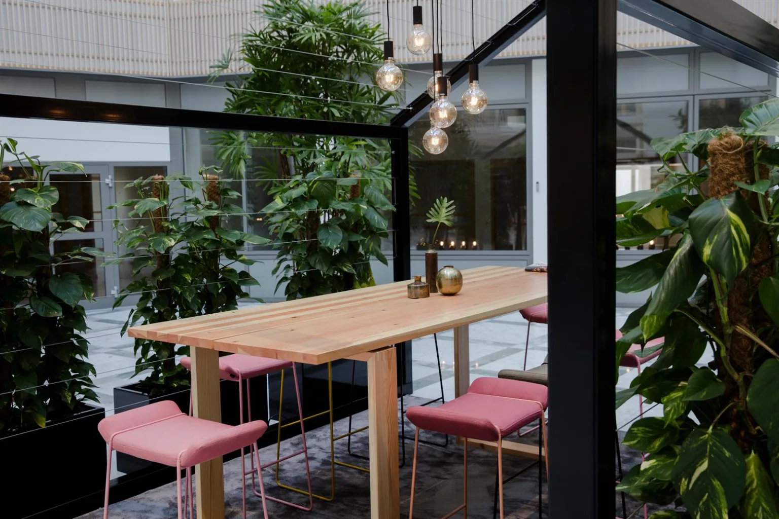 2. Ett uterum med trämöbler, rosa sittdynor och omgivande växtlighet.