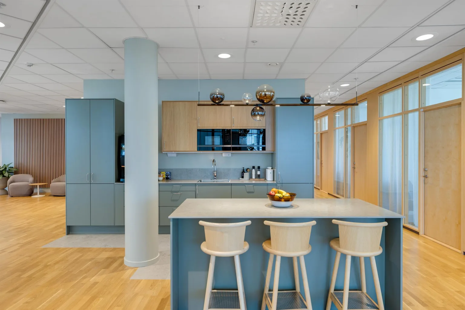 3. Modernt kök med blåa skåp, en köksö med tre stolar och en skål med frukt.