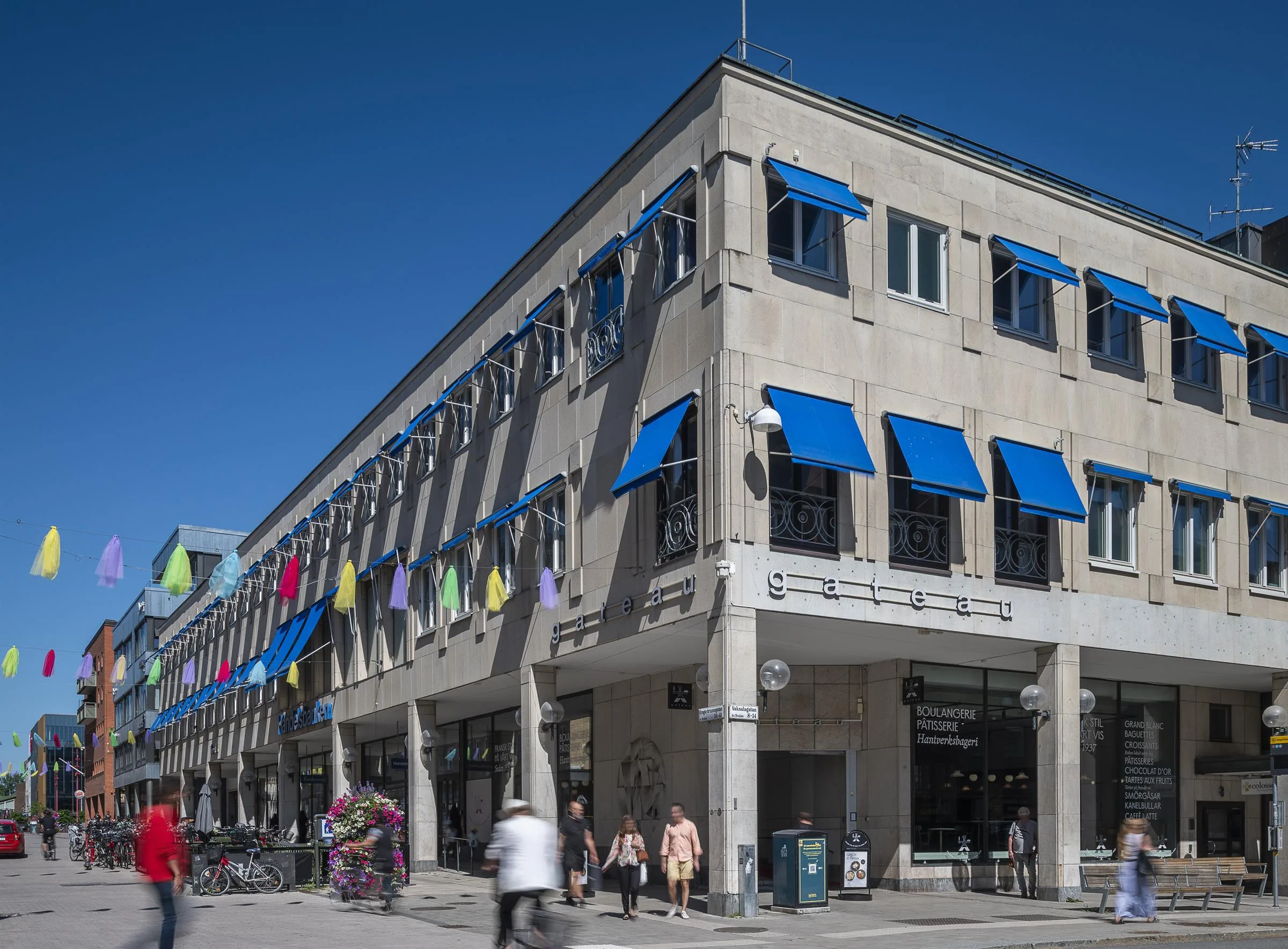 4. En modern byggnad med blå markiser och färgglada vimplar, omgiven av folk som promenerar.