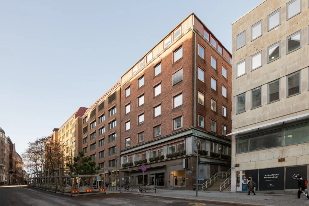 5. En byggnad med fasader i rödbrunt tegel och glasfönster, med trottoar och affärer på marknivå under en ljus himmel.