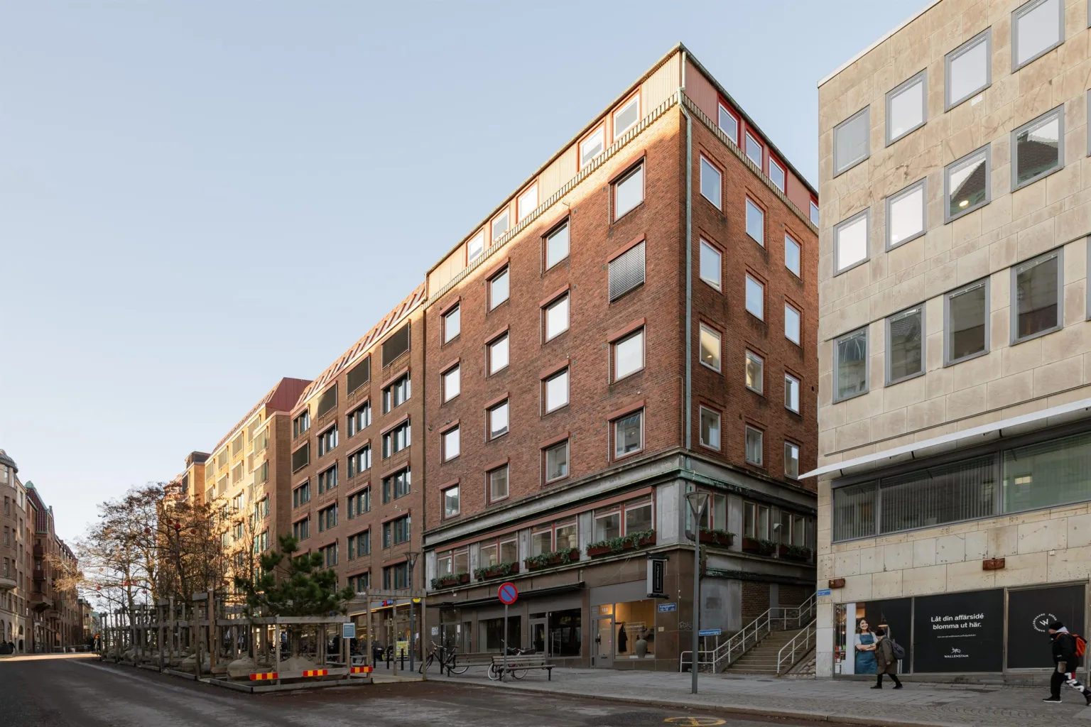 5. En byggnad med fasader i rödbrunt tegel och glasfönster, med trottoar och affärer på marknivå under en ljus himmel.