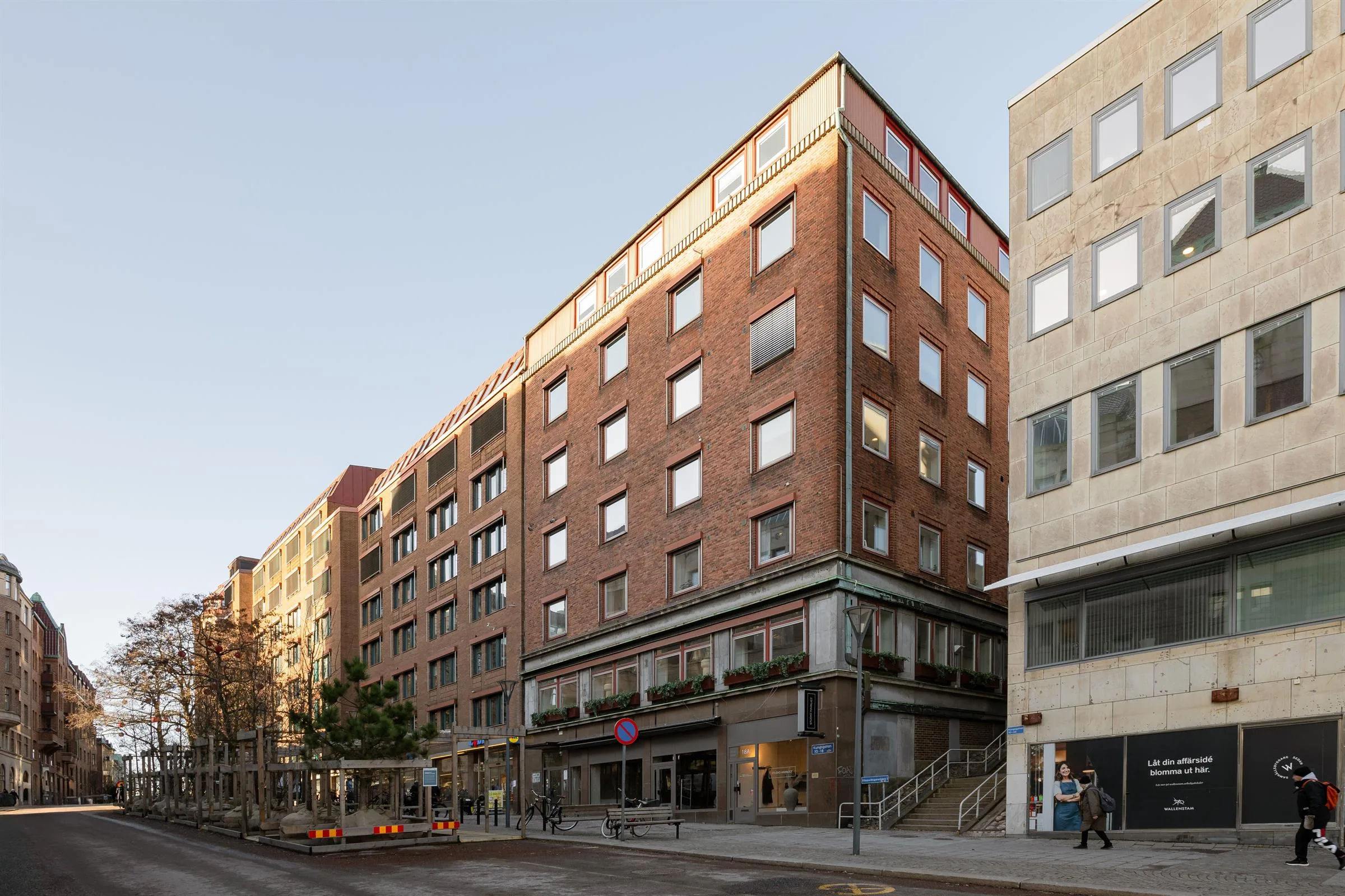 5. En byggnad med fasader i rödbrunt tegel och glasfönster, med trottoar och affärer på marknivå under en ljus himmel.