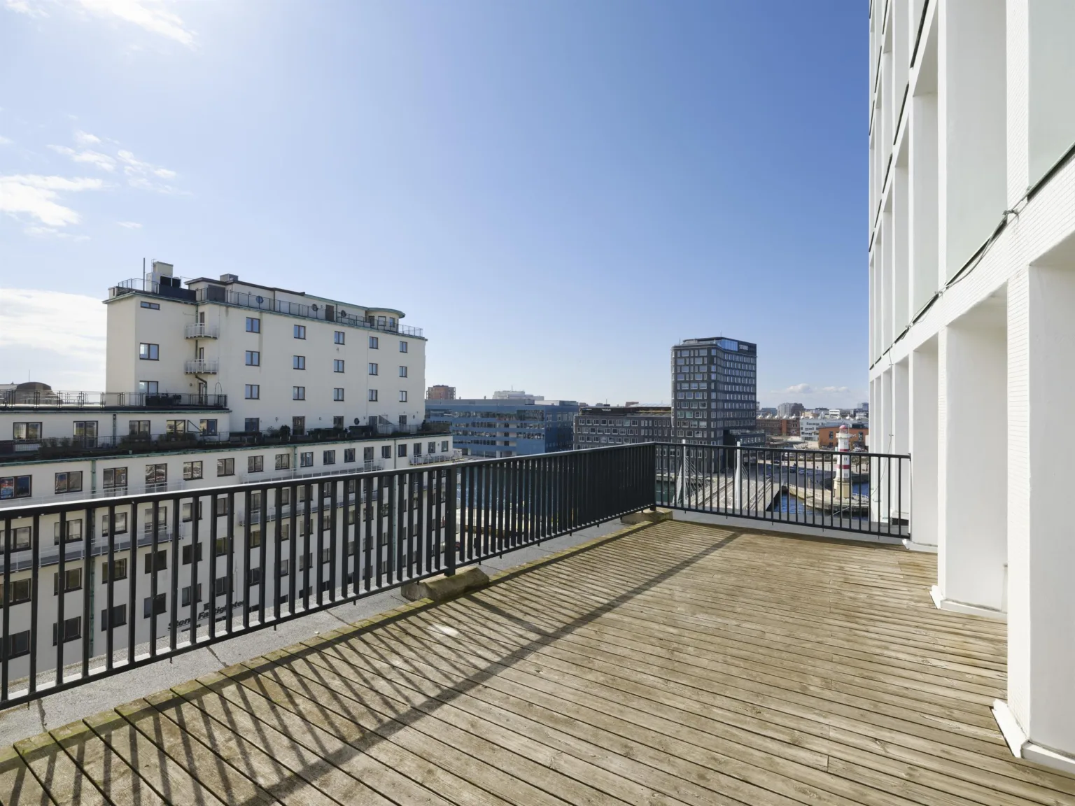 En takterrass med trägolv och utsikt över stadens byggnader under en klarblå himmel.
