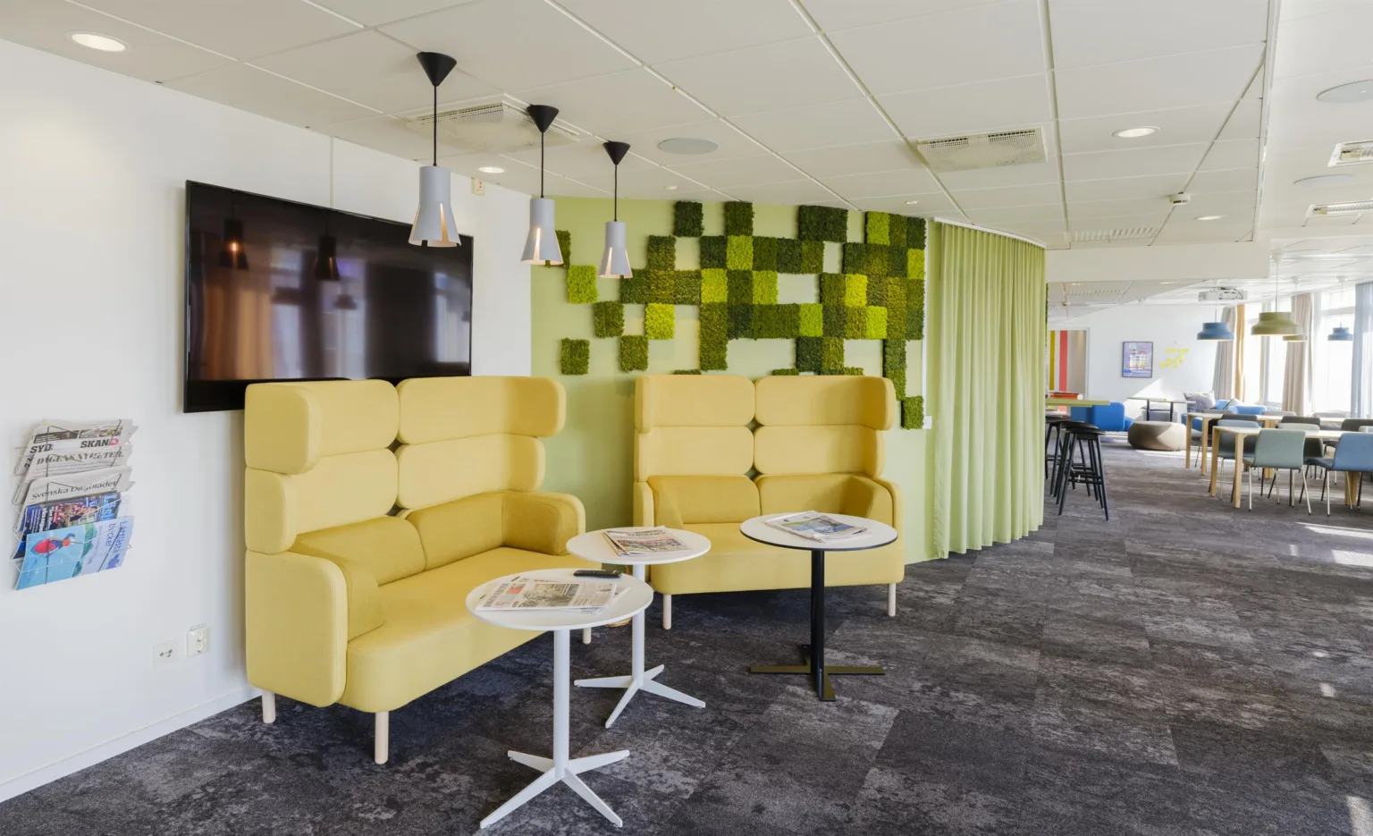 2. En lounge med gula fåtöljer, små runda bord och en grön väggdekoration i bakgrunden.