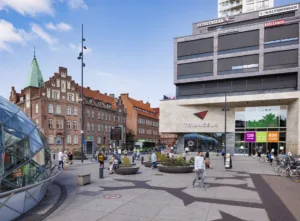 En stadsmiljö med moderna och historiska byggnader, människor som rör sig och cyklar.