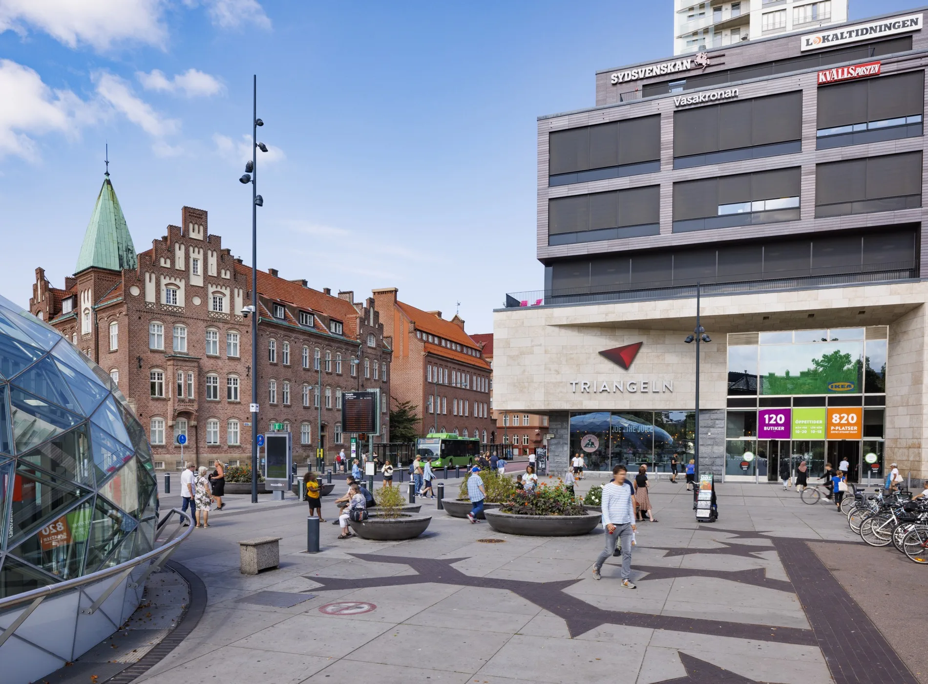 En stadsmiljö med moderna och historiska byggnader, människor som rör sig och cyklar.