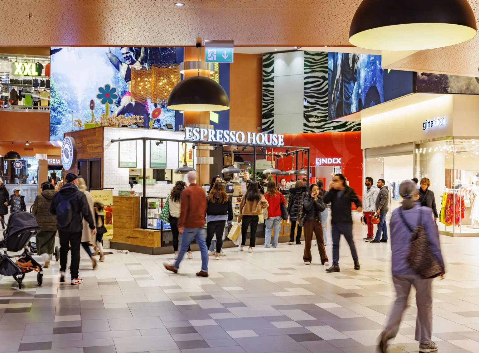En livlig inomhusmiljö på ett köpcentrum med människor som passerar och Espresso House i bakgrunden.