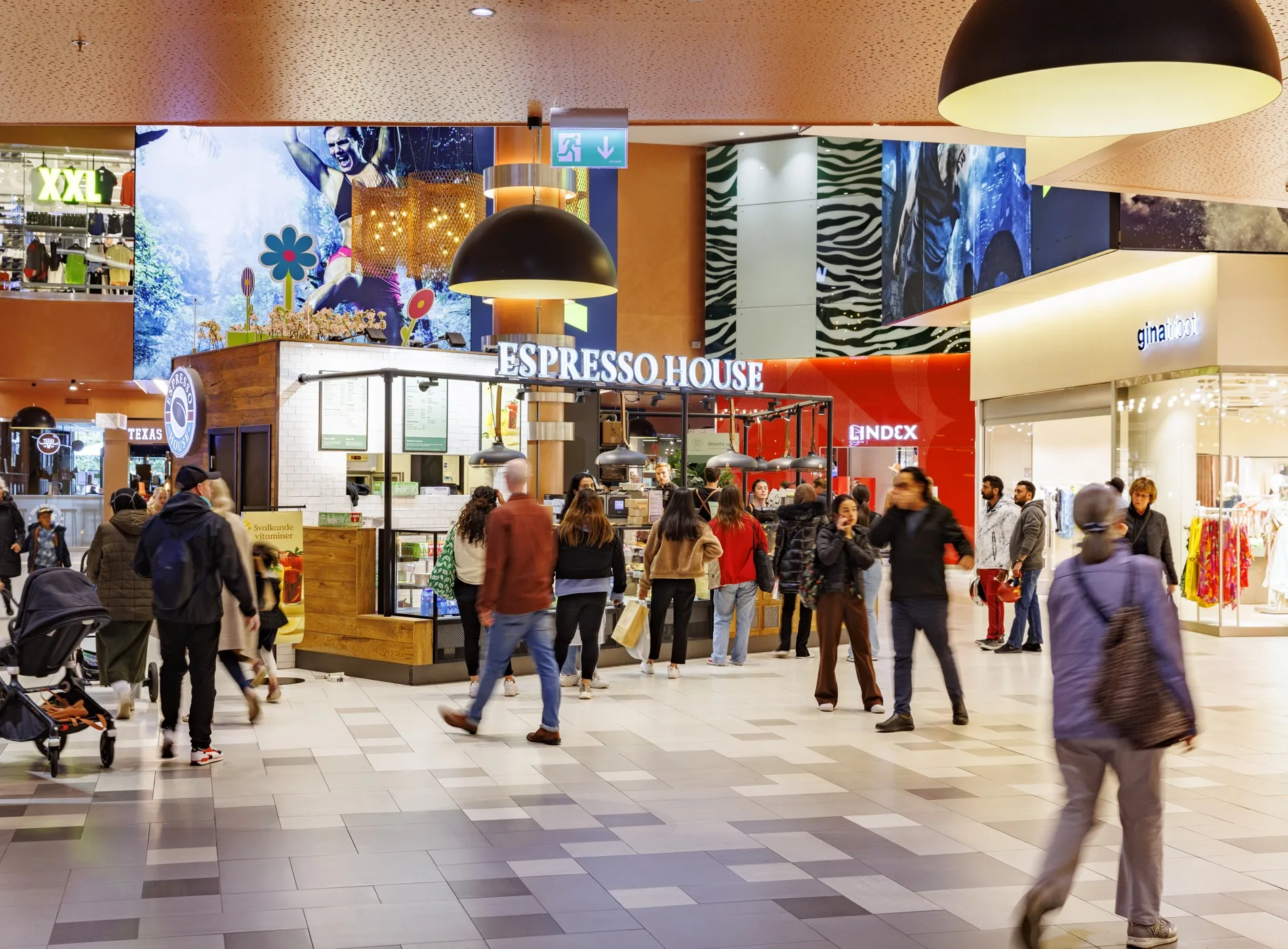En livlig inomhusmiljö på ett köpcentrum med människor som passerar och Espresso House i bakgrunden.