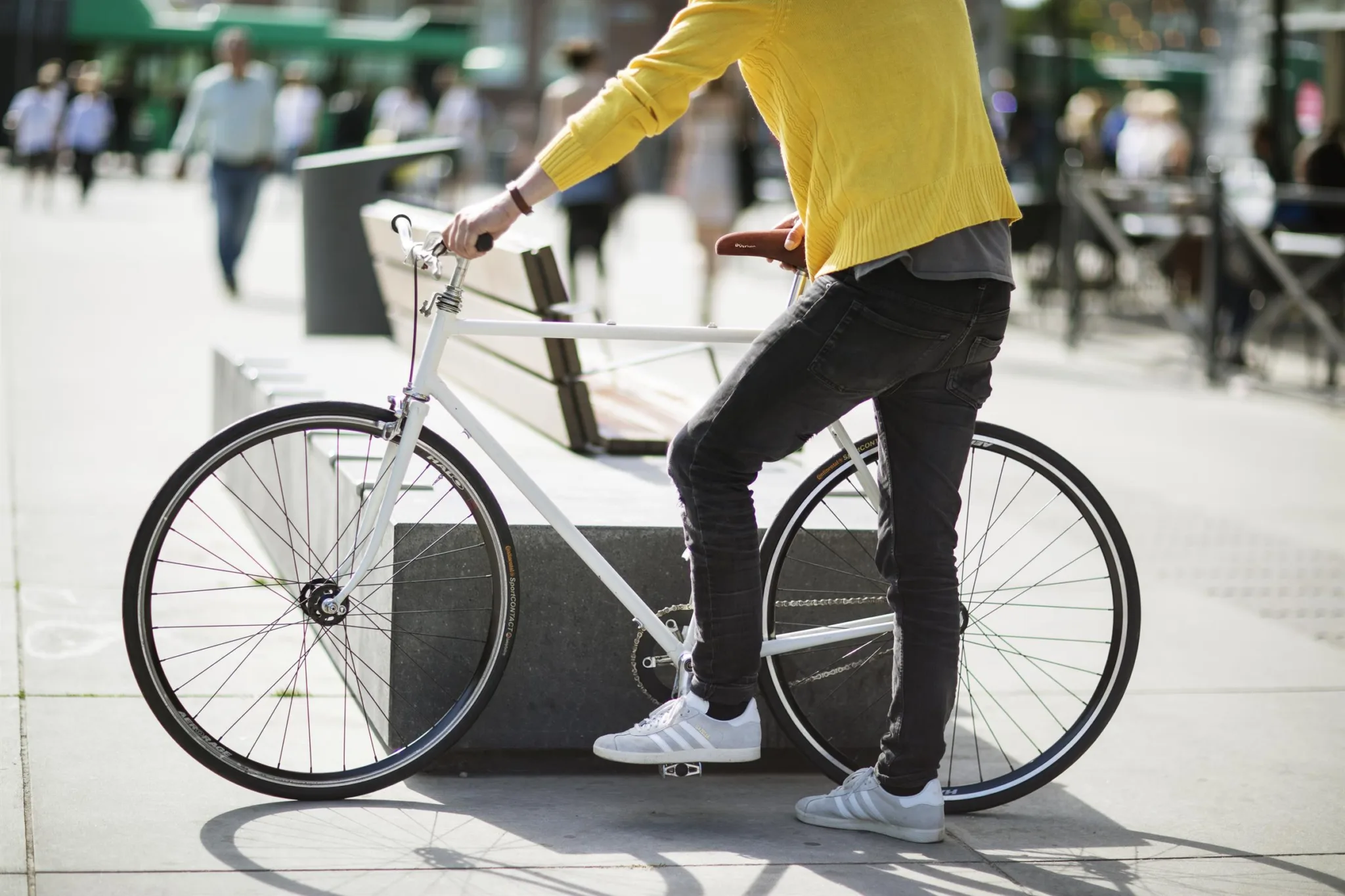 En person i gul tröja står med en vit cykel på en stadsgata.