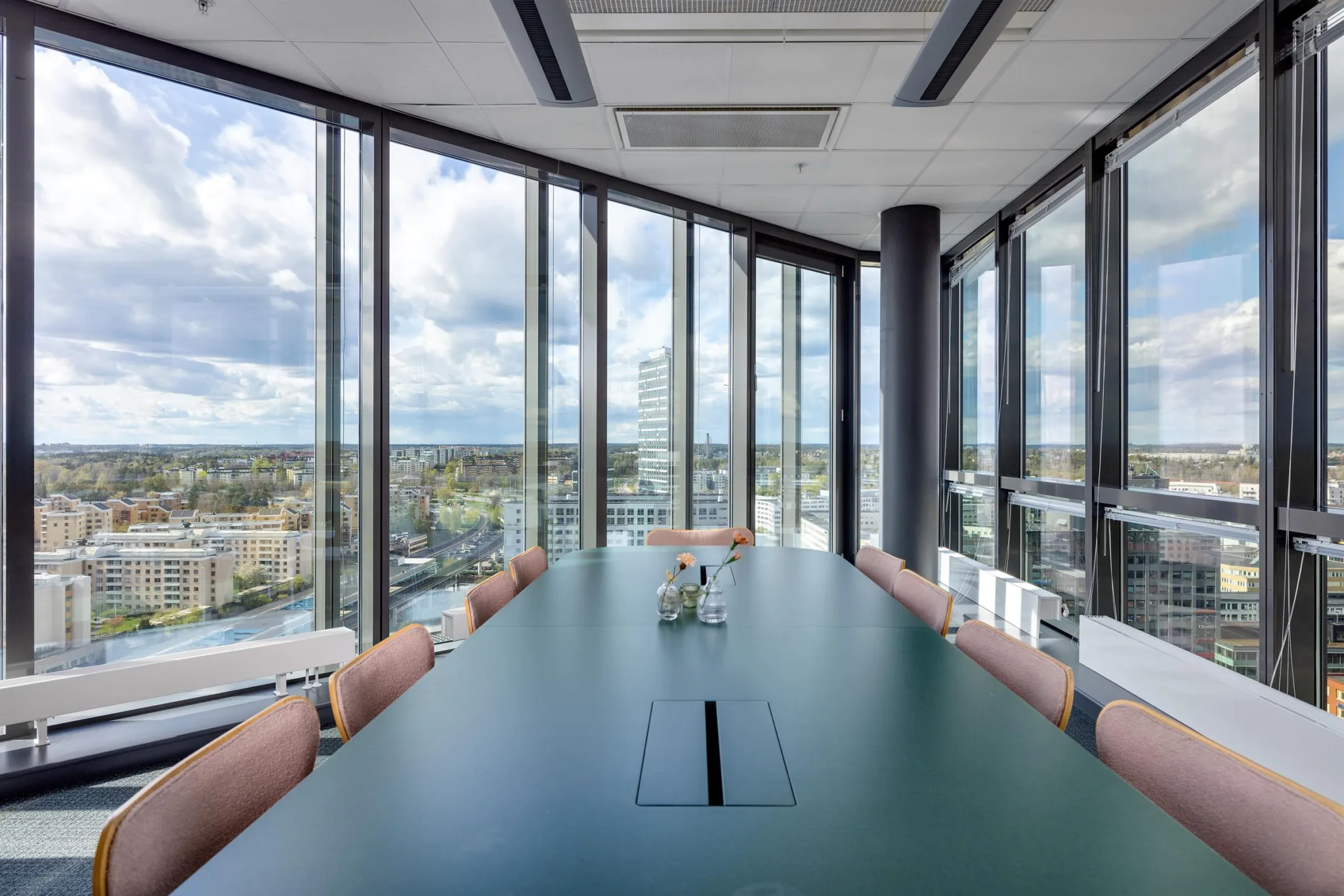 Ett konferensrum med ett långt bord, rosa stolar och stora fönster som ger utsikt över en stad.