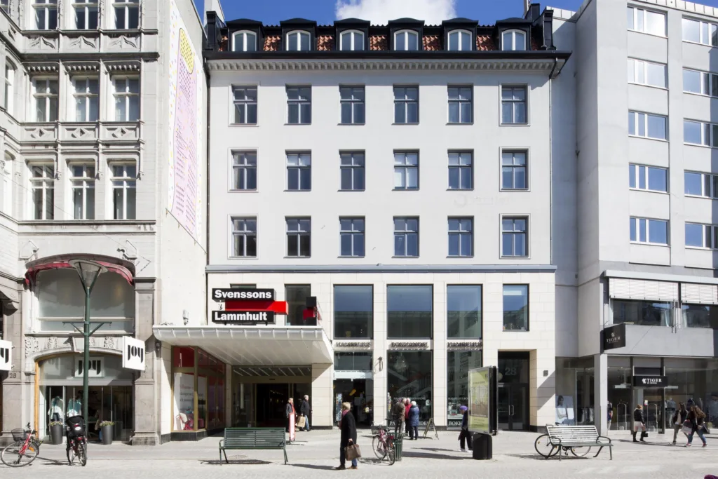 Vit byggnad med stora fönster och en skylt med texten "Konditori" ovanför entrén, flera personer står utanför.