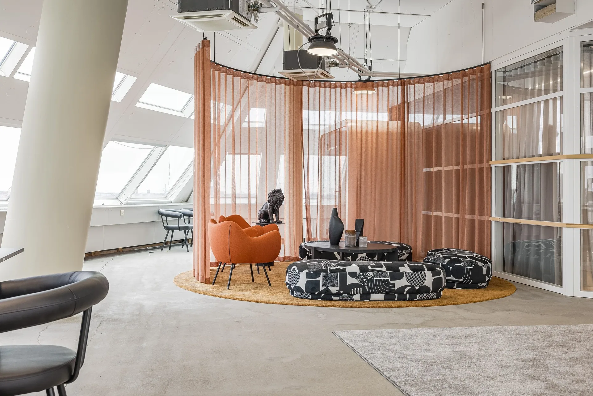 En modern lounge med orange fåtölj, mönstrade sittpuffar och skärmväggar i tyg.
